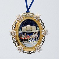 A detailed gold-tone metal ornament depicting a snowy winter sleigh ride. A horse-drawn carriage carries a couple through an intricate archway of frosted trees and architectural elements, suspended by a blue ribbon.