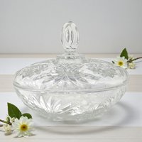 A clear glass serving dish with a matching lid featuring a starburst and pineapple pattern. The bowl has a scalloped rim and a pedestal-like base, while the lid is topped with a faceted pointed finial.
