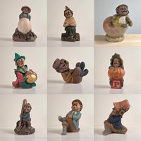 A grid of nine individual photos showcasing various resin gnome and character figurines by artist Tom Clark. The figures include a gnome leaning on a large egg, one sitting on a wooden log, a character emerging from a seashell, a gnome painting a large gold ornament, a laughing figure reclining, a gnome sitting on a pumpkin atop a red block, a baseball-themed gnome with a bat, and two figures designed as shelf-sitters.