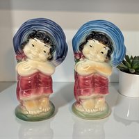 A ceramic planter shaped like a cheerful boy wearing a large wide-brimmed sun hat and red robes. The glazed figure has a high-gloss finish with visible fine crazing, standing on a small green base with arms folded.