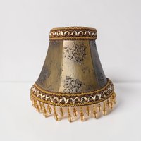 A small, hexagonal clip-on lampshade with a weathered bronze-gold metallic finish and textured distressing. The top and bottom are trimmed with ornate braided cord, featuring amber-colored crystal teardrop beads dangling from the lower rim.