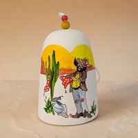 A hand-painted ceramic bell featuring a clown figure in cowboy gear. The clown wears a tan western hat, a red neckerchief, and a yellow suit with red polka dots.