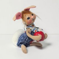 Tan felt bunny in a sitting pose with a large white pom-pom tail. He wears denim overalls and a blue and white striped kerchief with an apple print. He holds a large glossy red apple. He has a joyful hand-painted face and pink-lined ears.