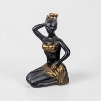 A vintage Italian matte black majolica decanter shaped like a kneeling woman in a graceful pose. She has lustrous gold-toned highlights on her wrap and jewelry and is positioned in profile, standing approximately 10 inches tall.