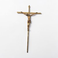 A slender, polished gold-tone metal crucifix with an ornate flared cross design. The figure of Christ is rendered in high relief with a small INRI plaque positioned at the very top of the vertical beam.