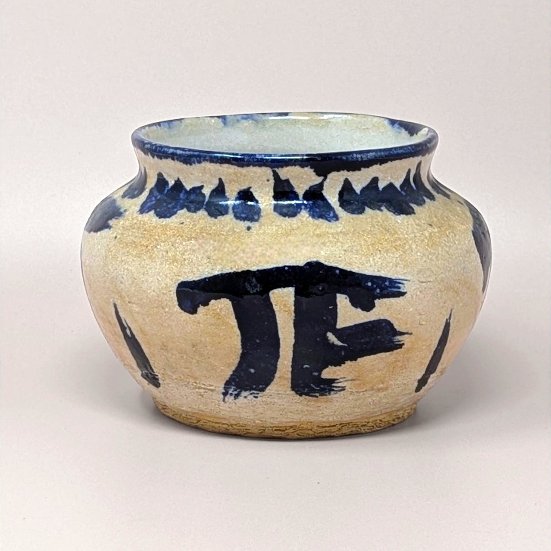 Hand-thrown pottery bowl with a globular shape and a sandy, textured tan glaze. Featuring bold, gestural cobalt blue brushstrokes including a large "PI" or "TF" symbol and a saw-tooth rim pattern.