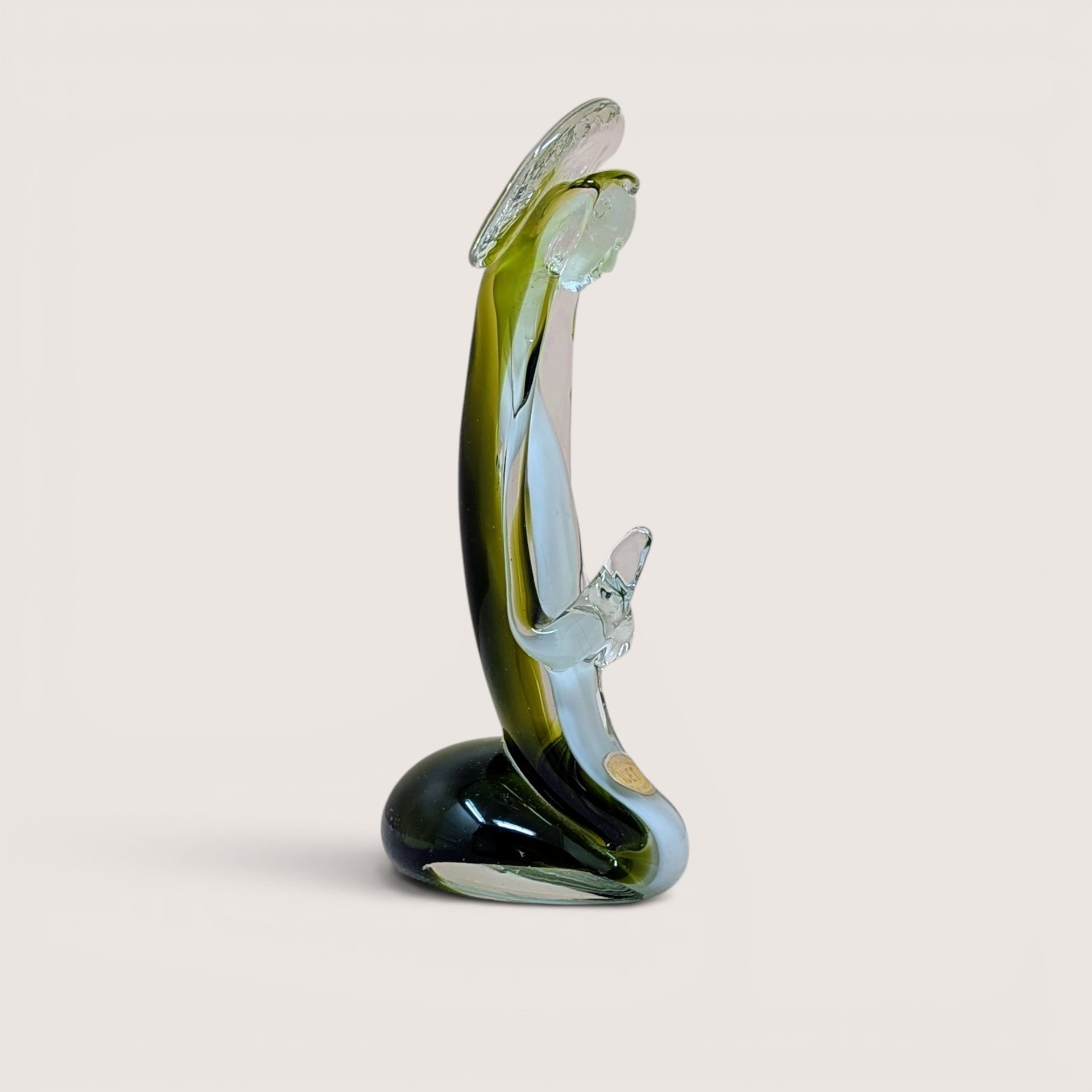 A vertical art glass sculpture of a person in a prayerful pose. A vibrant green inner layer is visible through the thick clear glass exterior, which curves into a stable, weighted base.