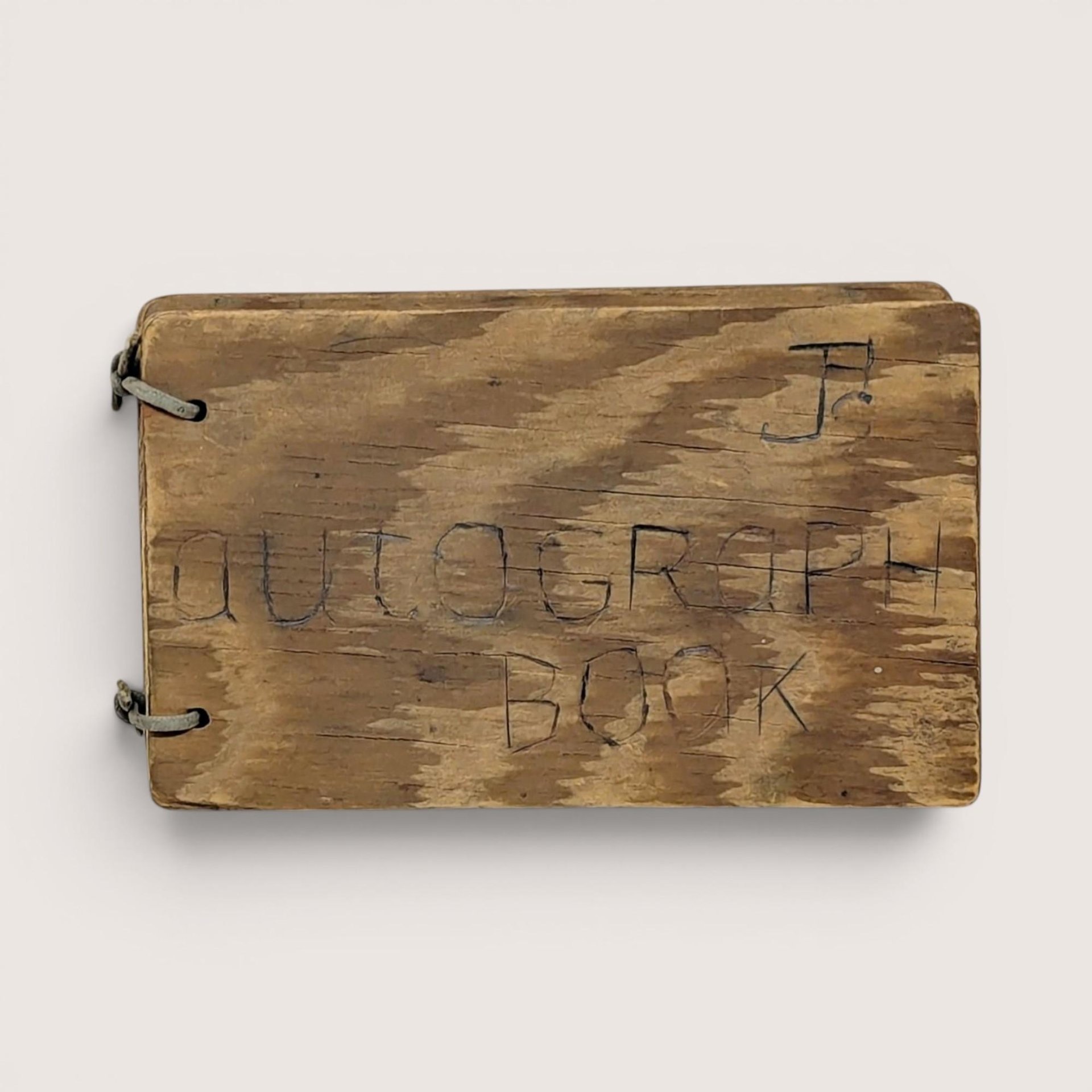 A small, rectangular autograph book with a natural wood grain cover. The words "Autograph Book" are hand-carved into the wood. Two metal rings bind the pages on the left. Rustic, weathered texture with a warm honey-oak finish.