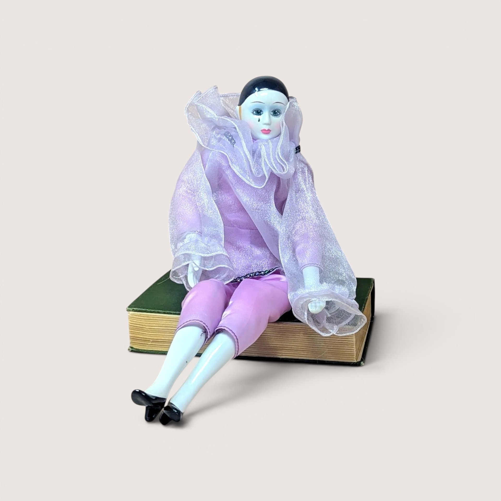 A 16-inch vintage Pierrot clown doll wearing a pink satin and sheer organza outfit, sitting on a green book against a neutral background.