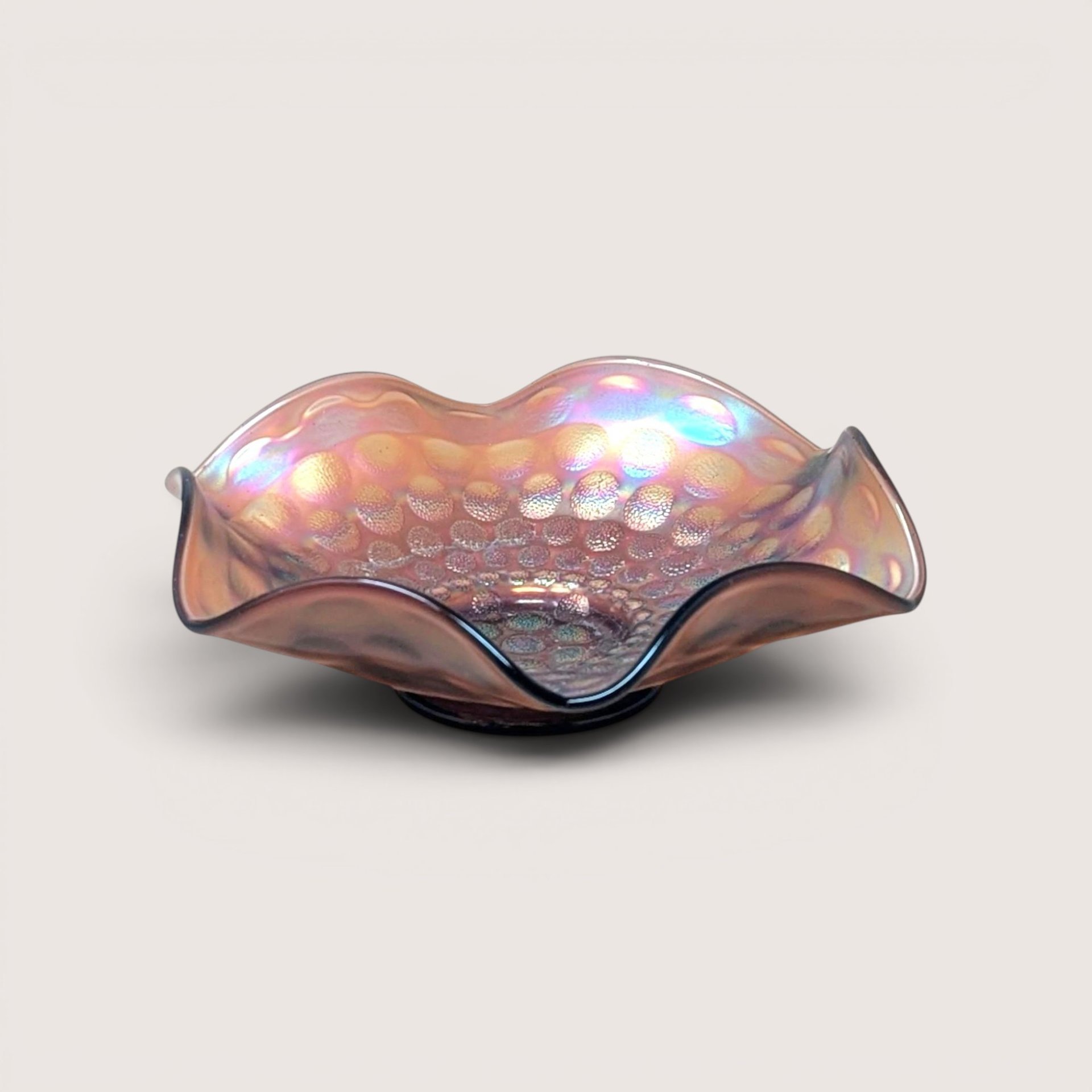 A vintage Fenton marigold carnival glass bowl with a ruffled edge and a dimpled coin dot pattern, showing iridescent pink and gold tones.