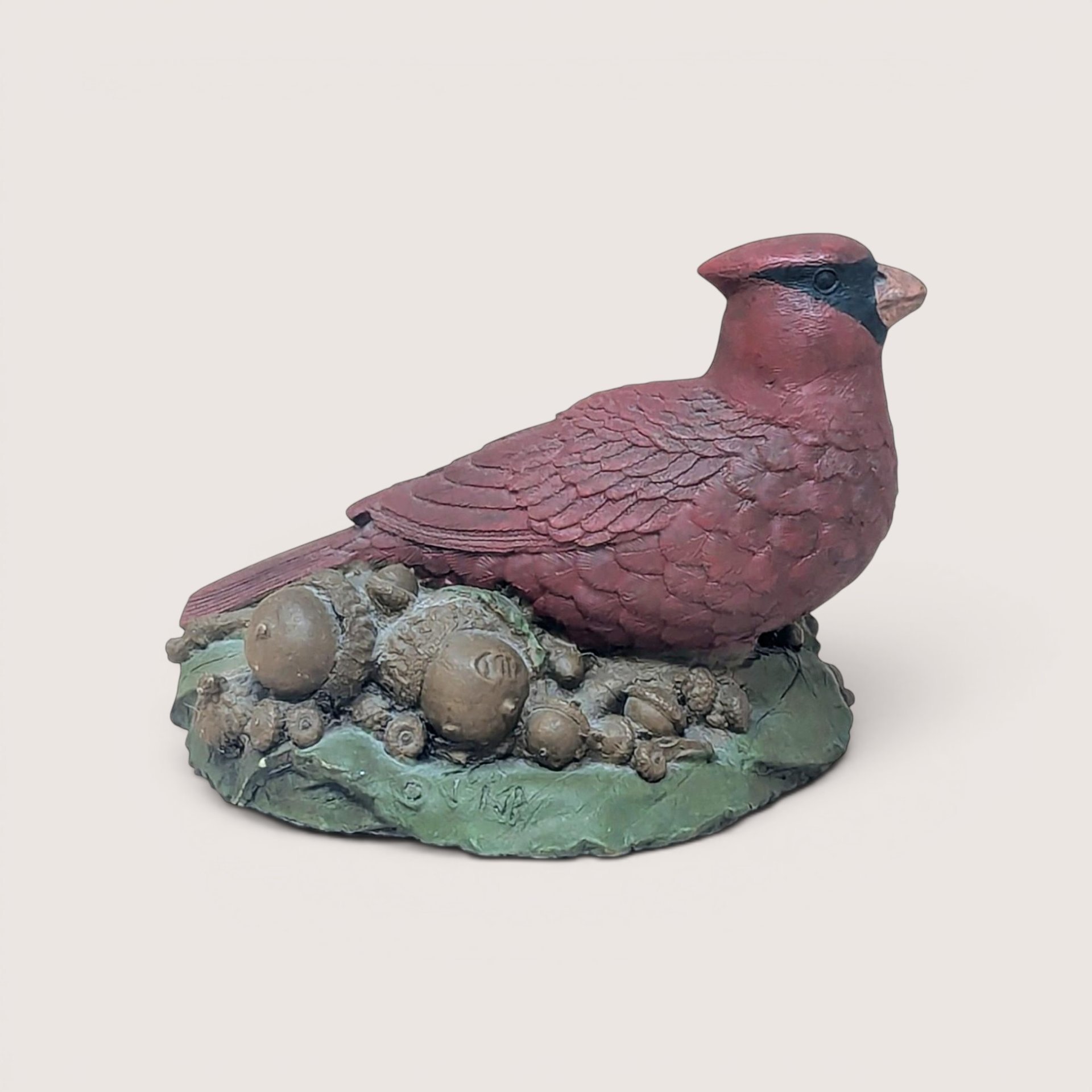 A hand-painted resin sculpture of a red cardinal perched on a bed of acorns and green leaves against a neutral background.