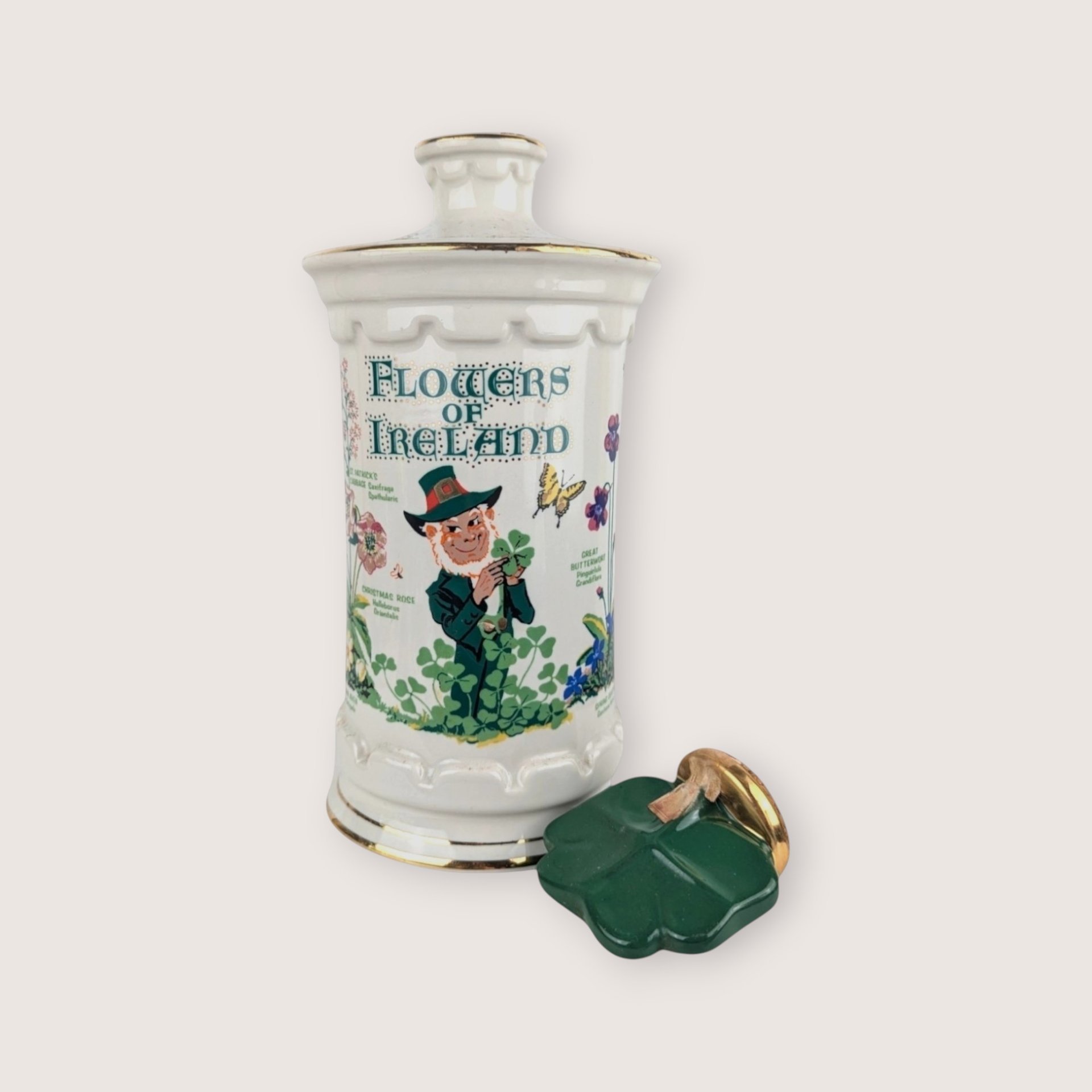 White ceramic empty liquor decanter with a Flowers of Ireland leprechaun design and a broken green shamrock stopper.