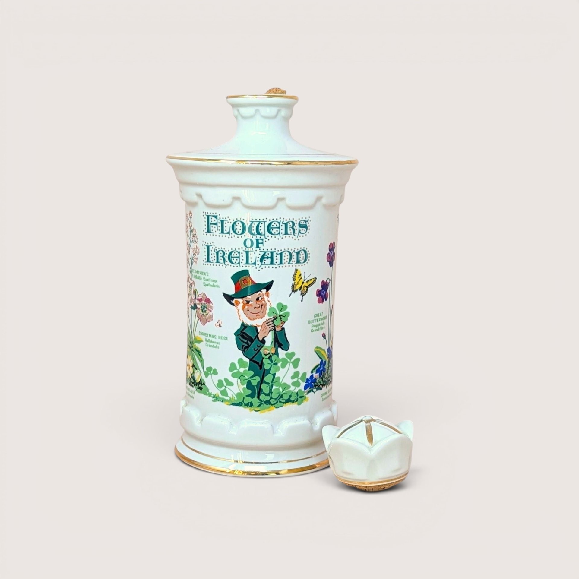 A white porcelain decanter featuring botanical "Flowers of Ireland" illustrations, a leprechaun figure, and a gold-trimmed flower-shaped stopper against a neutral background.