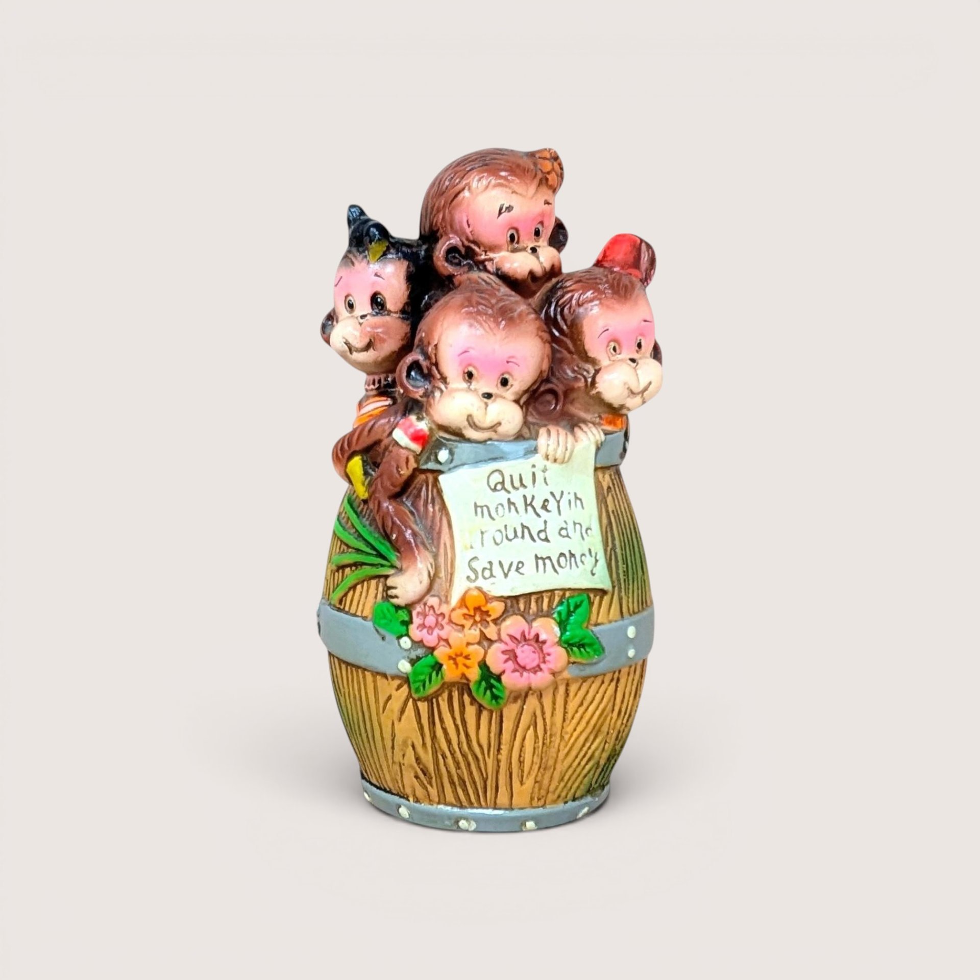 Vintage monkey coin bank peeking out of a barrel with flowers and a sign that reads Quit monkeyin round and save money.