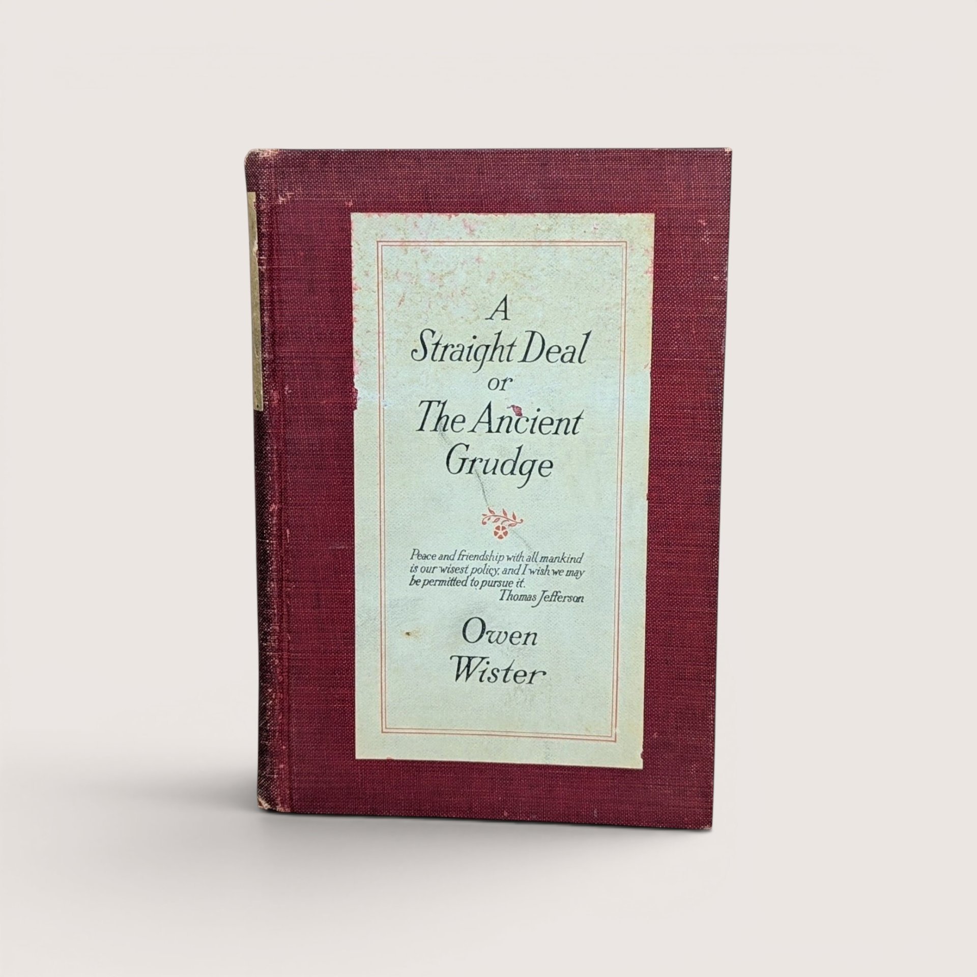 An antique book titled A Straight Deal or The Ancient Grudge by Owen Wister with a maroon cloth cover and cream paper label.
