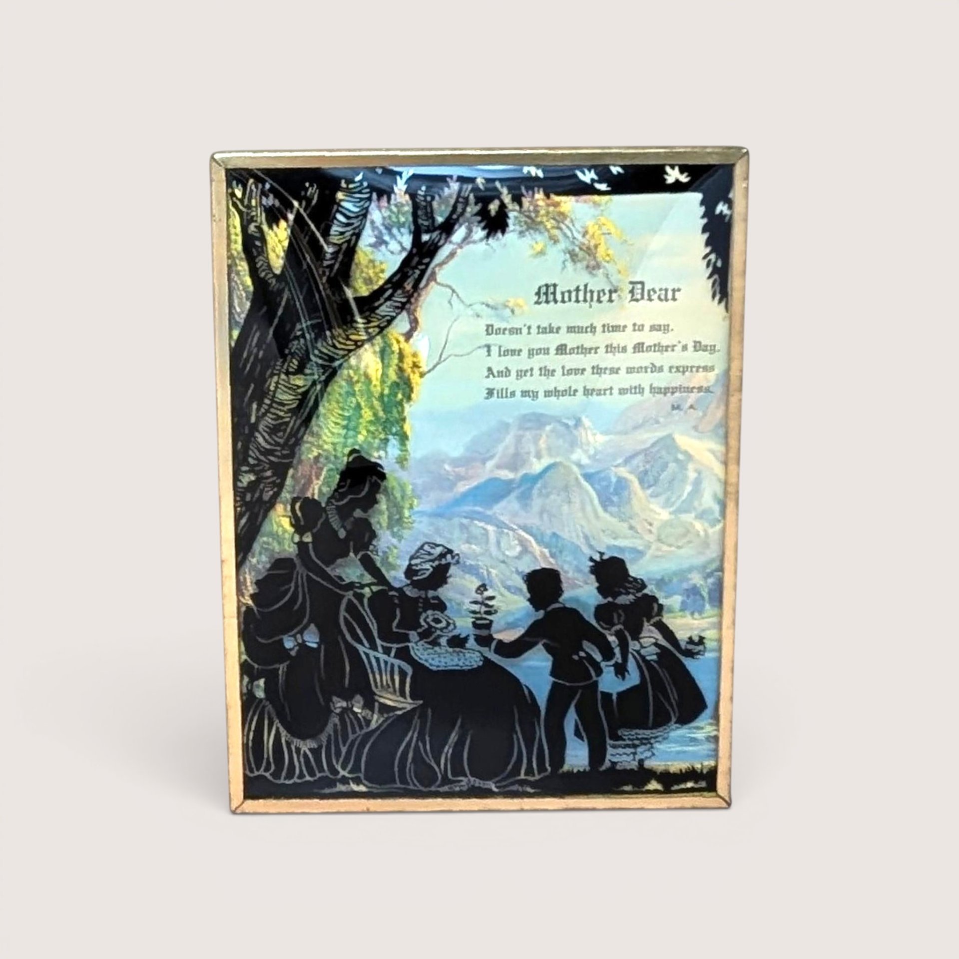 Vintage silhouette art of a family outdoors against a mountain backdrop, in a gold metal frame on a neutral background.