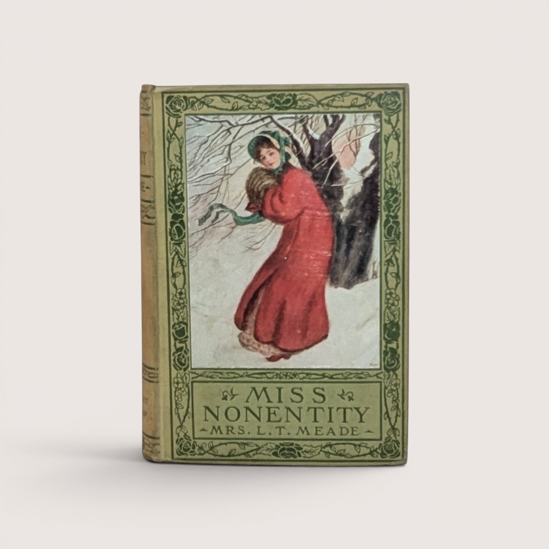 A vintage hardcover book titled Miss Nonentity by Mrs. L.T. Meade, featuring a pictorial cover of a woman in a red winter coat against a snowy background with green floral borders.