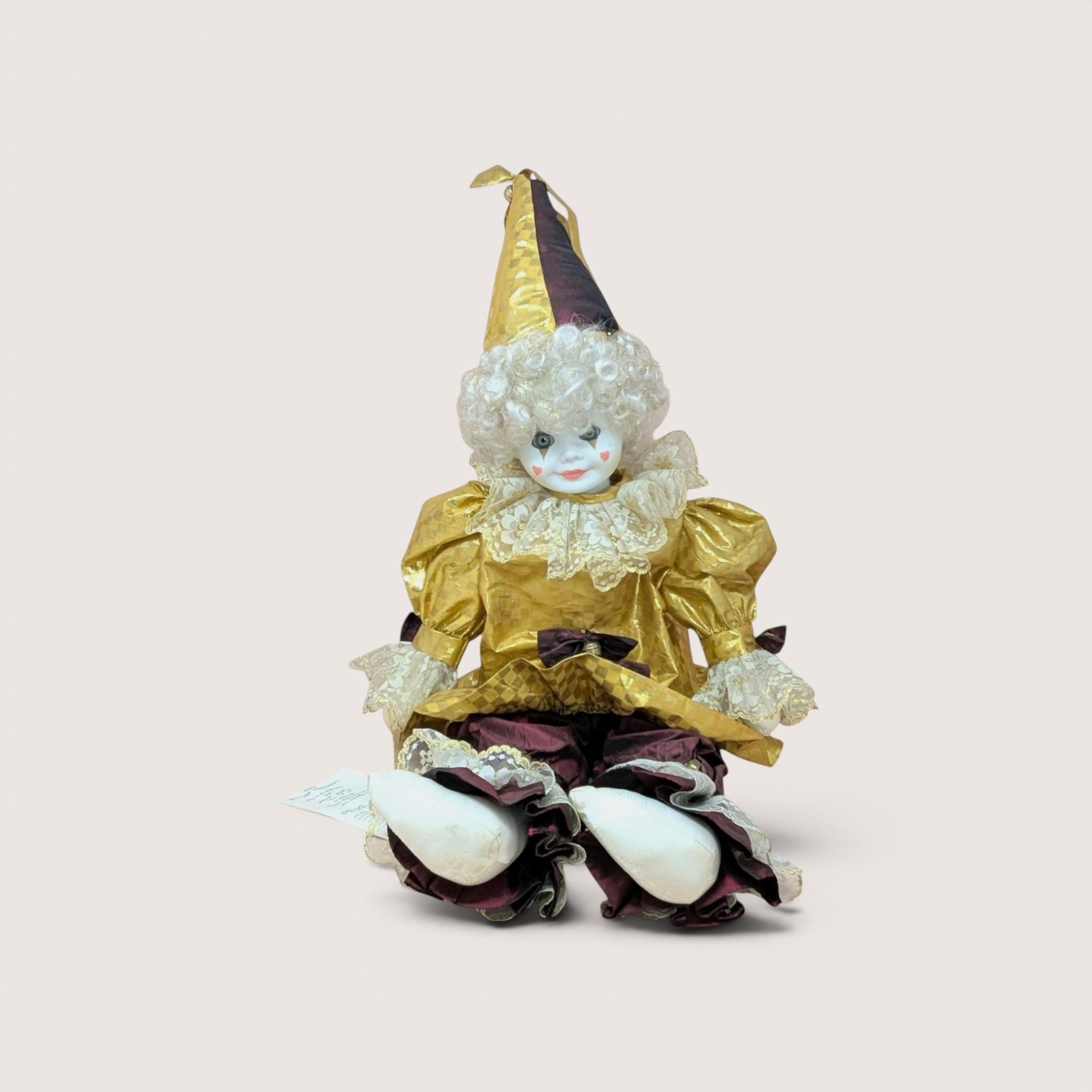 A large porcelain clown doll in a metallic gold and burgundy costume, wearing a tall pointed hat and featuring a white curly wig and hand-painted face.