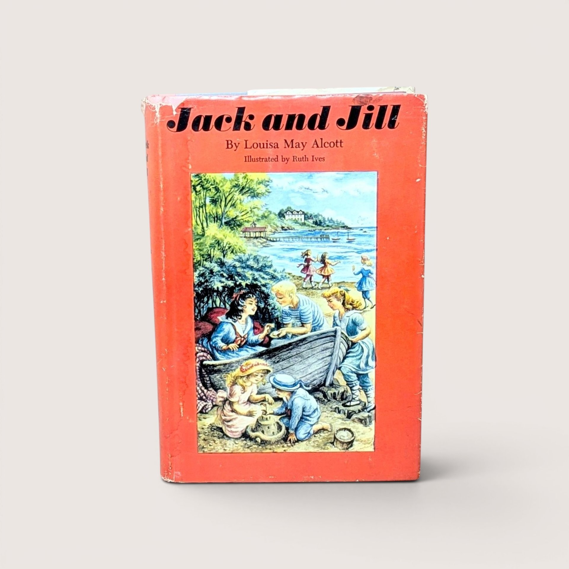 A vintage 1956 hardcover edition of Jack and Jill by Louisa May Alcott with a bright red dust jacket featuring children playing at the beach