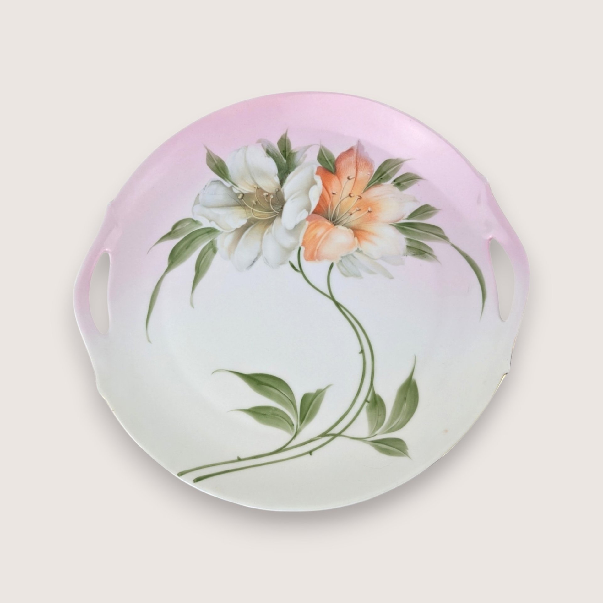 Antique Bavarian porcelain handled cake plate with hand painted orange and white flowers on a pink blush gradient background.