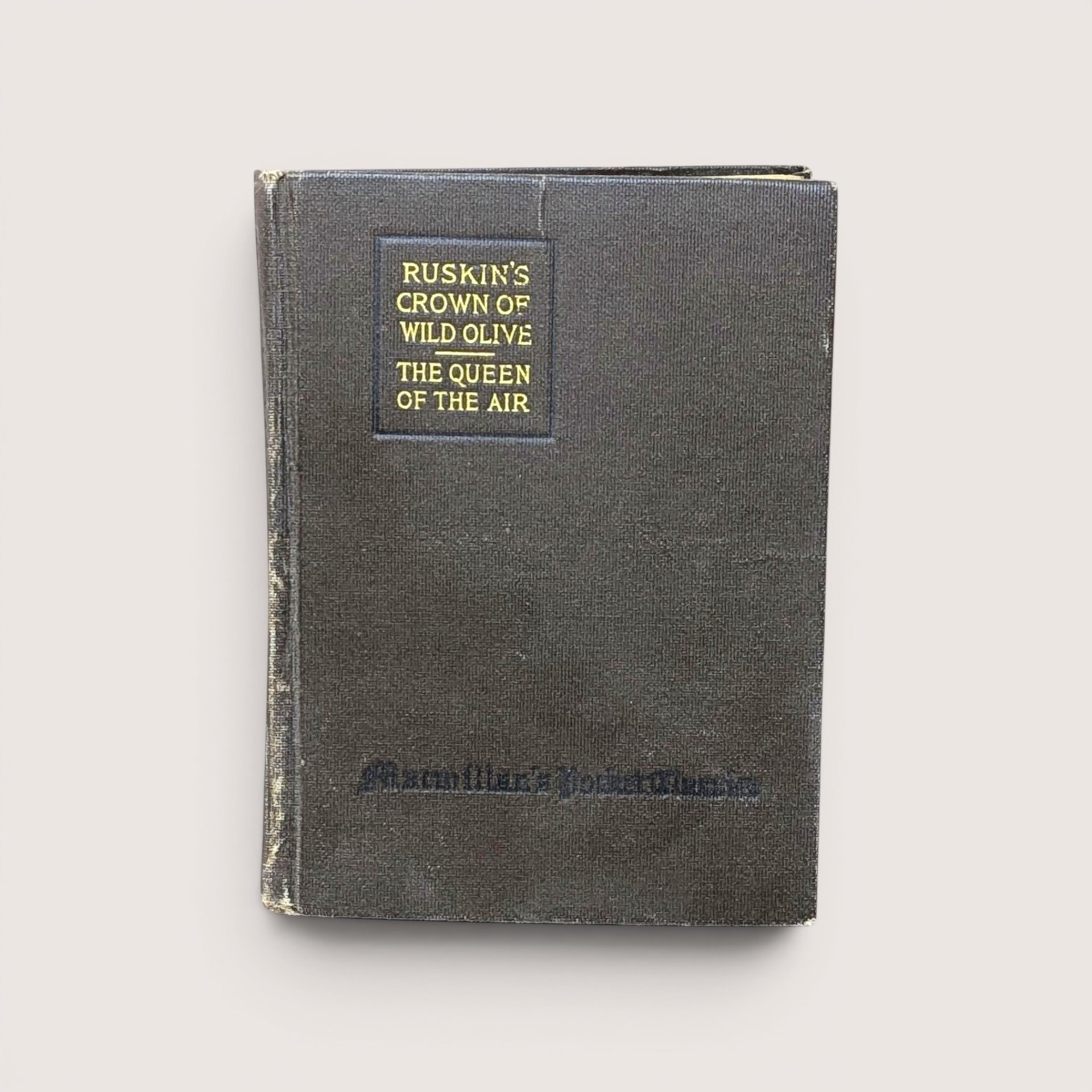 An antique dark cloth book cover titled "Ruskin's Crown of Wild Olive" in gold lettering, centered on a beige background.