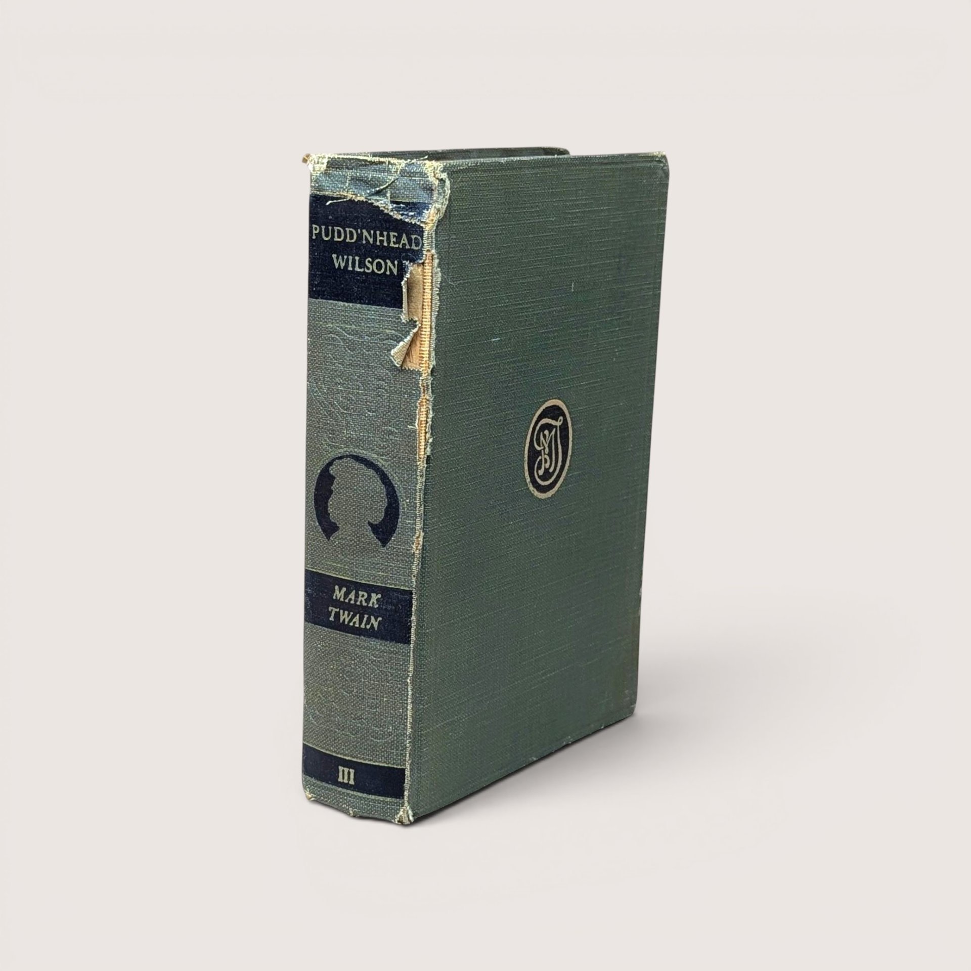 An antique worn green book spine titled "Pudd'nhead Wilson" by Mark Twain, angled on a beige background.