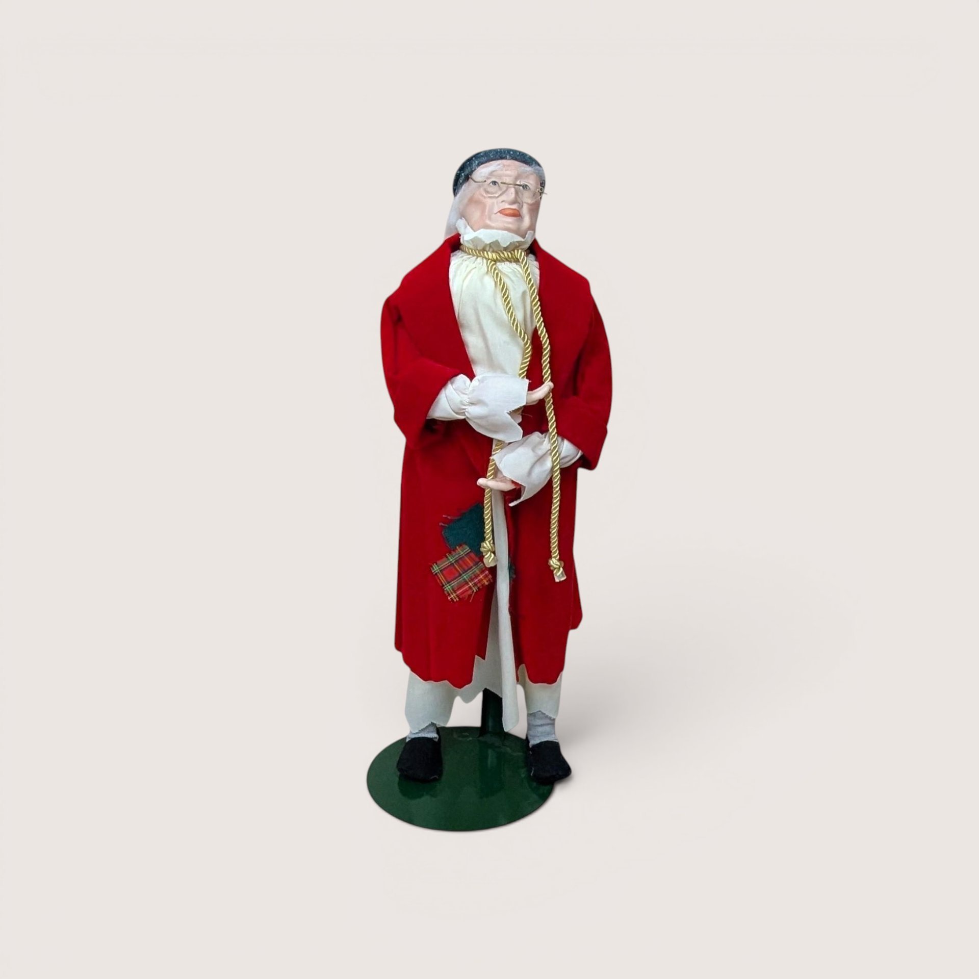 An elderly man doll wearing a red robe, spectacles, and a nightcap on a stand, centered on a beige background.