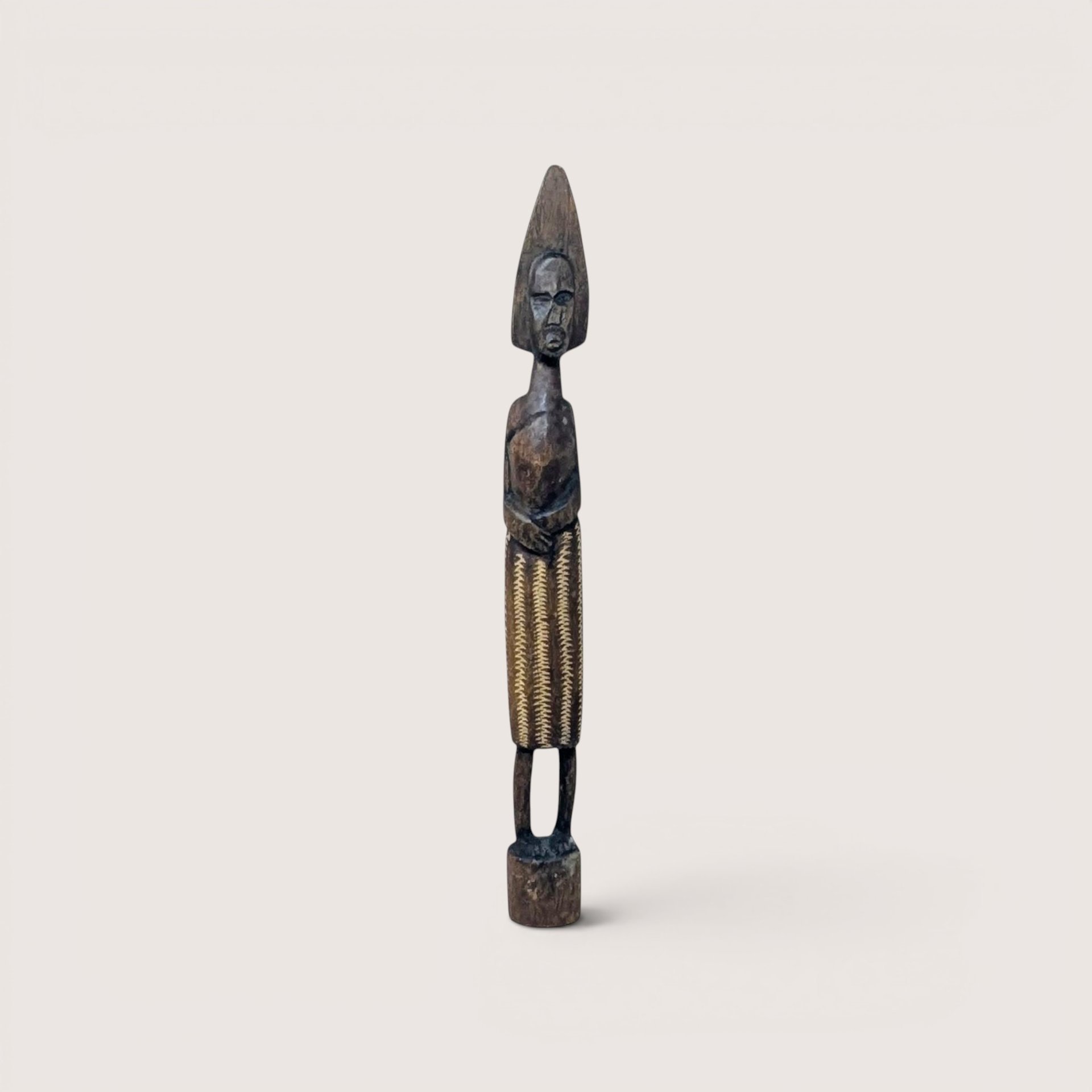 A slender, carved dark wood African style figurine with textured details, centered on a beige background.