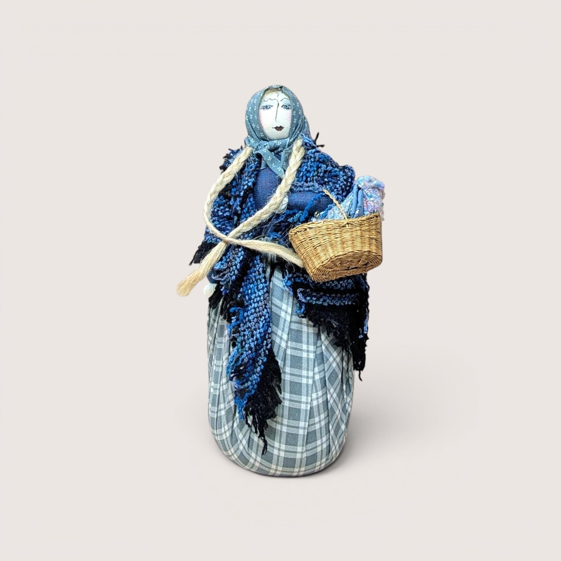A handcrafted textile doll with long black hair holding a small basket, centered on a beige background.