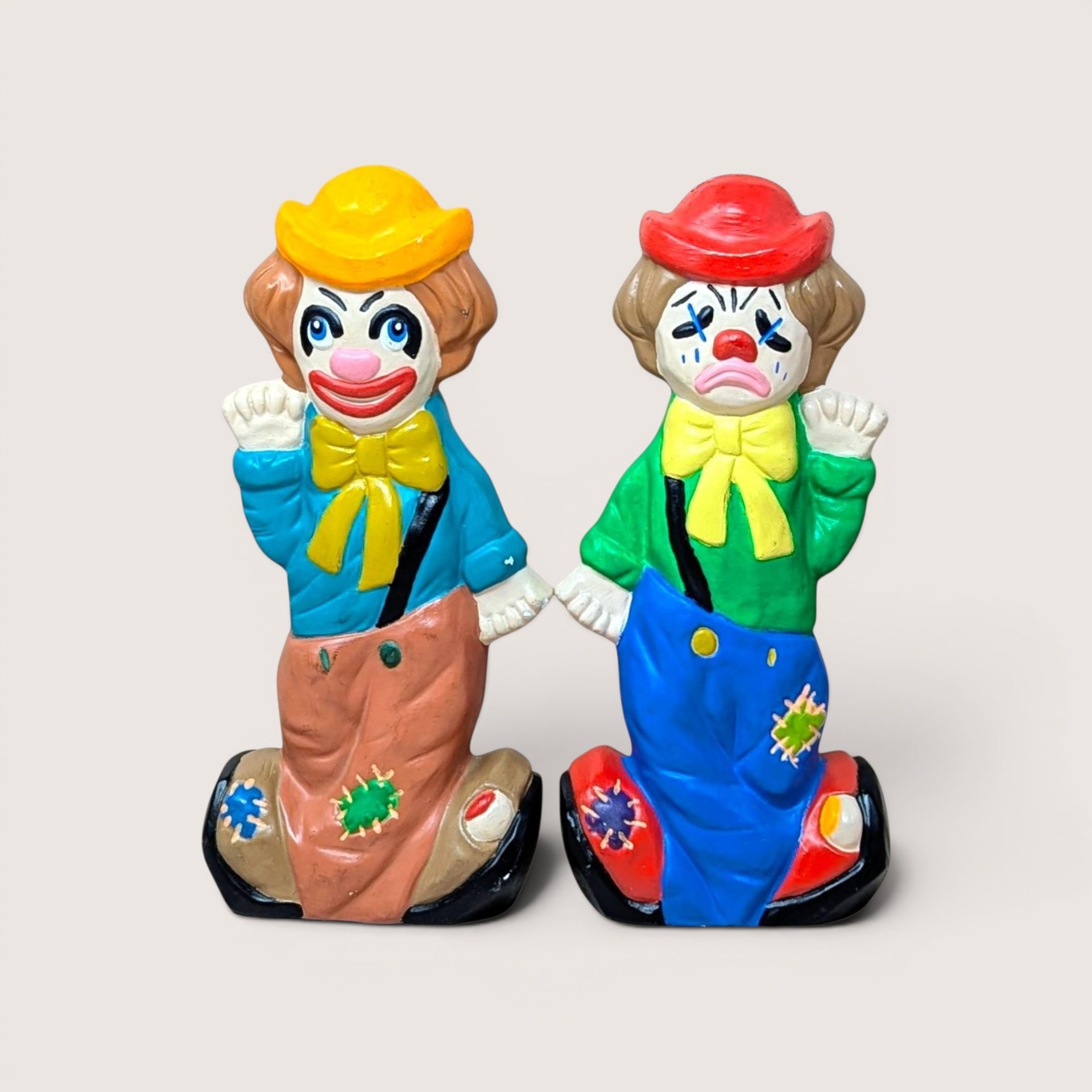 A pair of vintage ceramic hobo clown coin banks on a plain background, one smiling in a blue shirt and one crying in green.