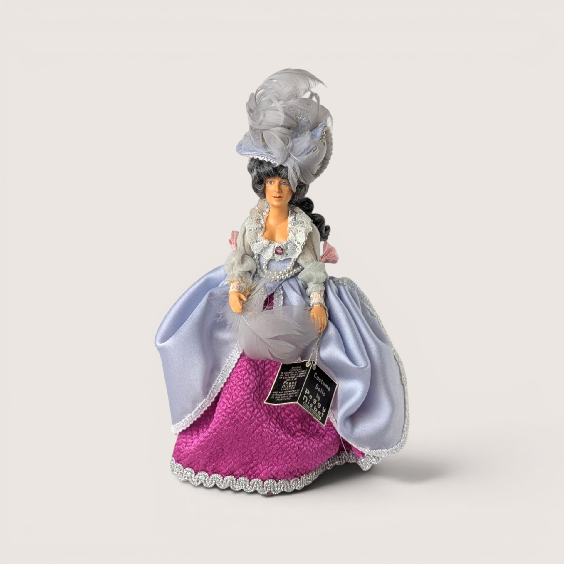 Vintage Peggy Nisbet Renoir portrait doll in an ornate lavender and pink gown with an elaborate feathered hat.