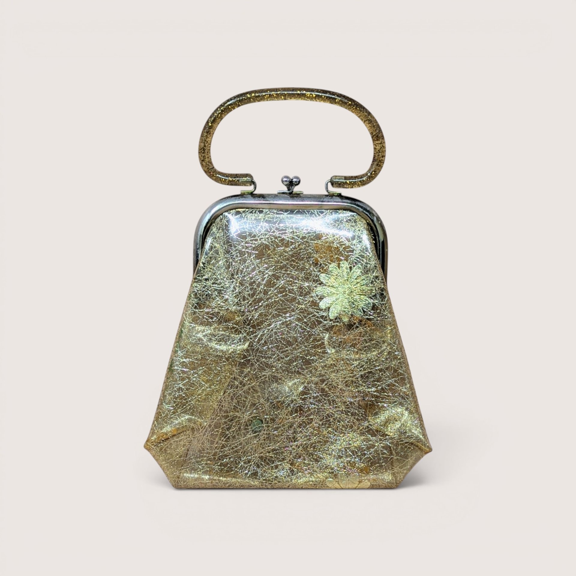 A vintage gold glitter lucite purse with a clear top handle and textured body, centered on a beige background.