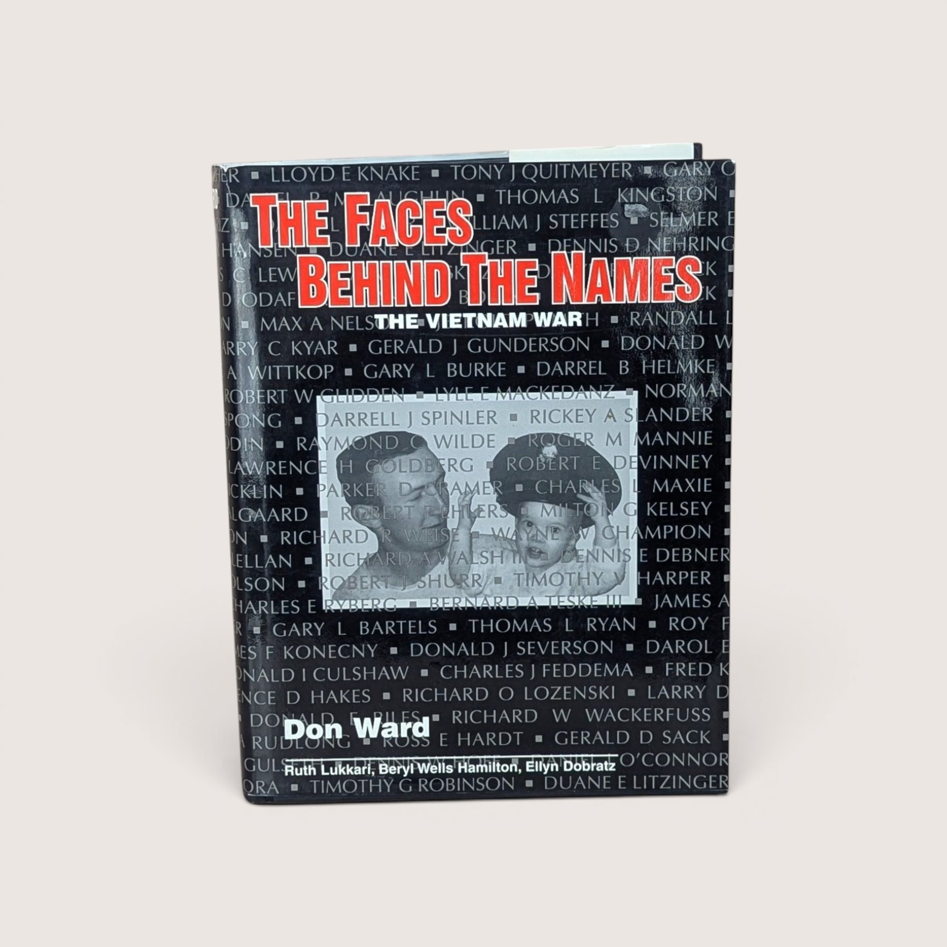 Hardcover book titled The Faces Behind the Names over a black dust jacket with military names and a central photo on a plain linen background.