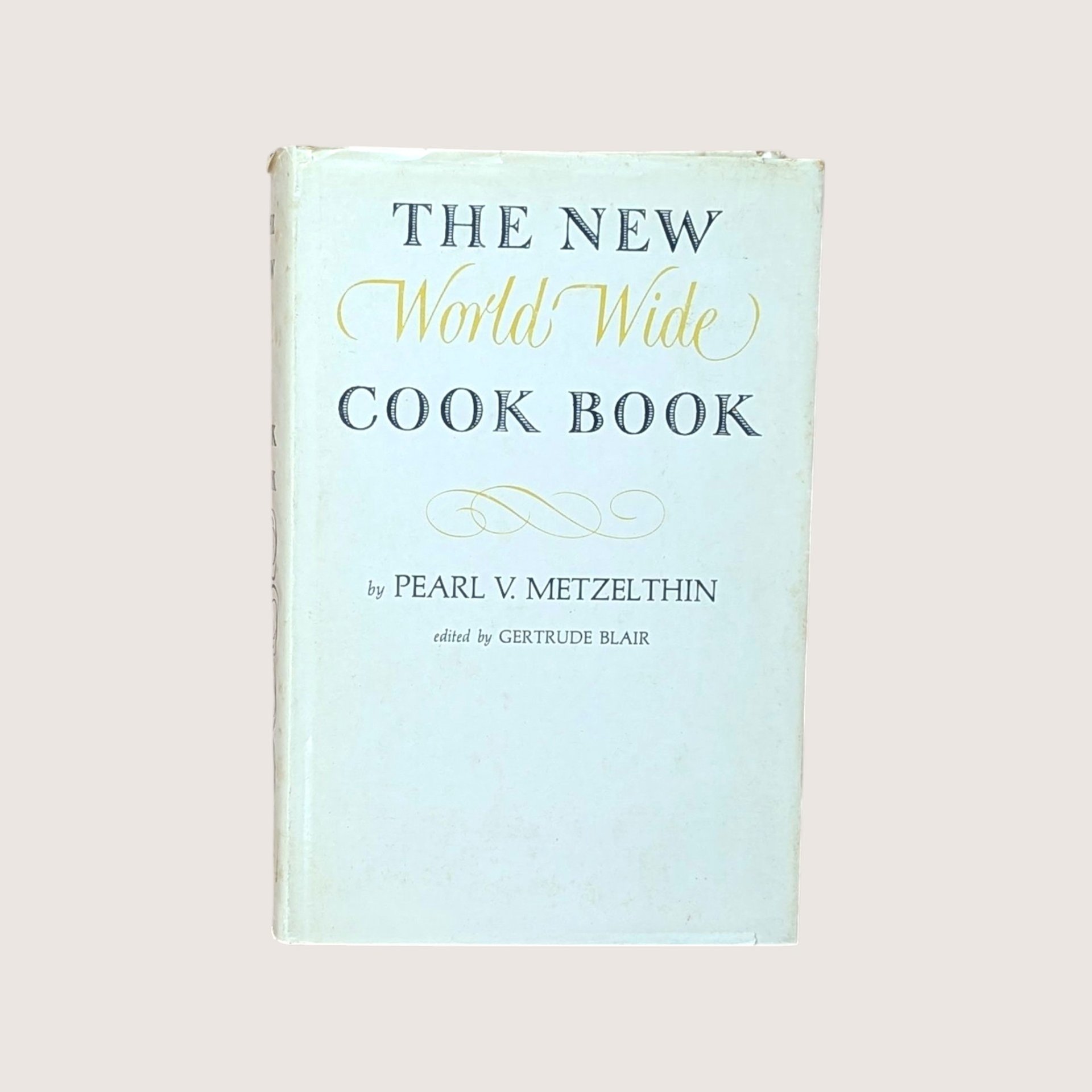 Vintage cookbook titled The New World Wide Cook Book by Pearl V Metzelthin centered on a plain linen background.
