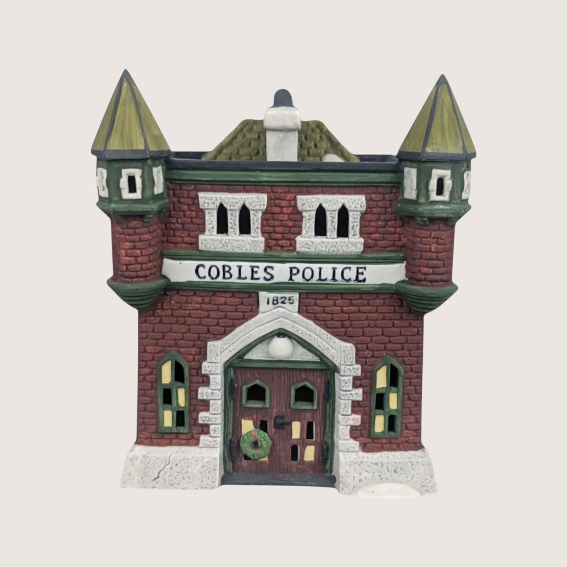 Dept. 56 Cobles Police Station ceramic building with a red brick facade and twin green turrets on a plain background.