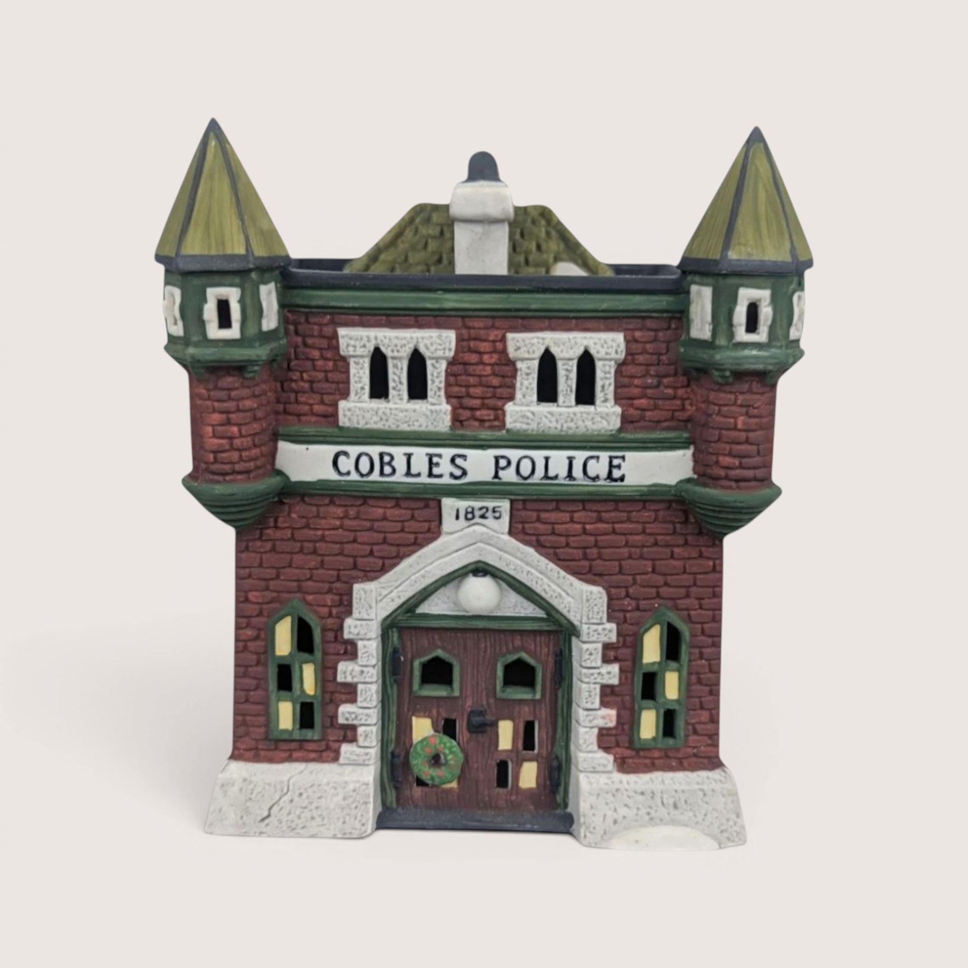 Dept. 56 Cobles Police Station ceramic building with a red brick facade and twin green turrets on a plain background.
