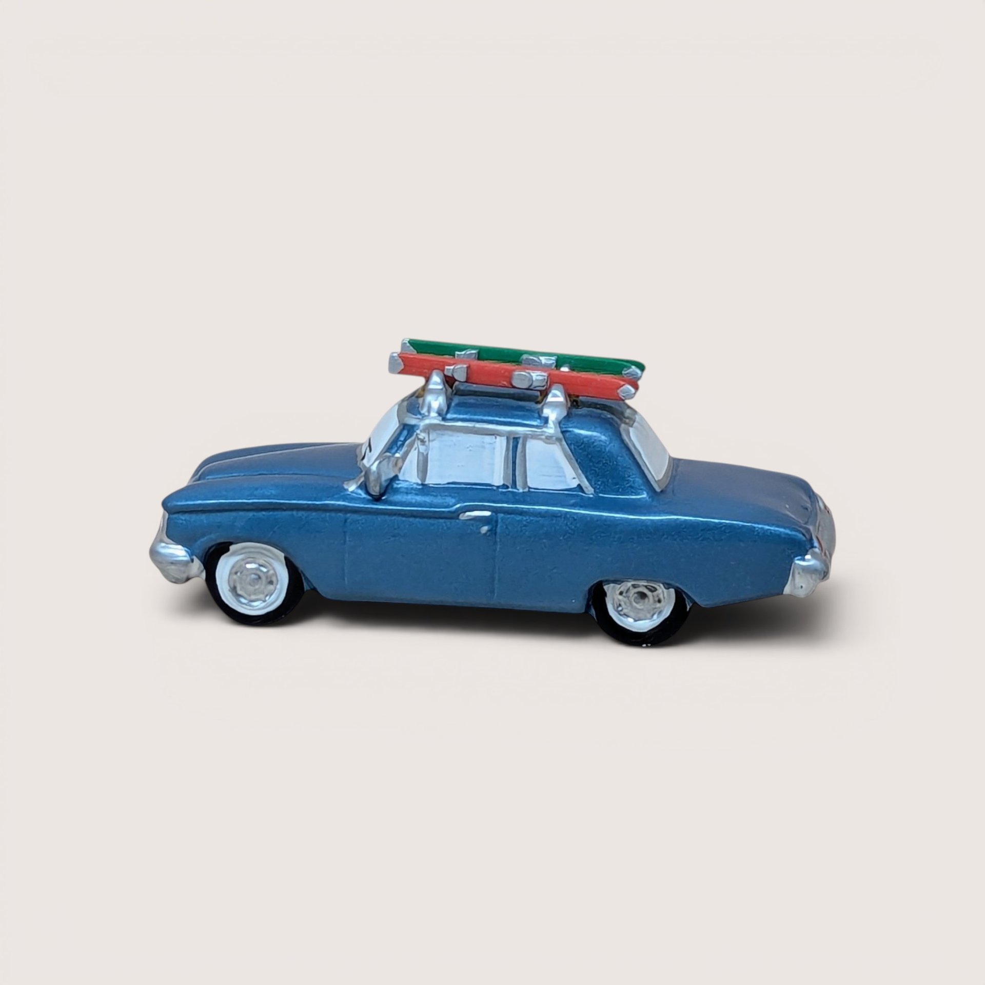 Vintage 1996 Department 56 Snow Village blue sedan car figurine with winter skis strapped to the roof rack.