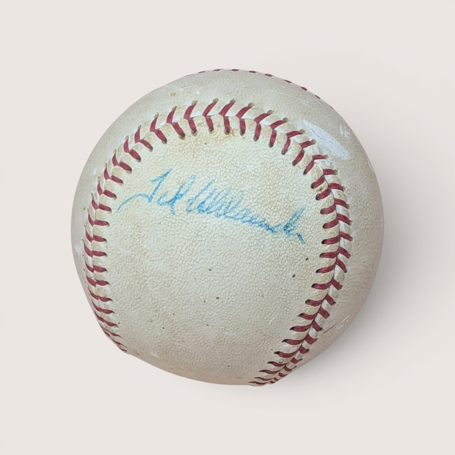 Vintage baseball with red stitching and a blue ink signature across the sweet spot, centered on a plain linen background.