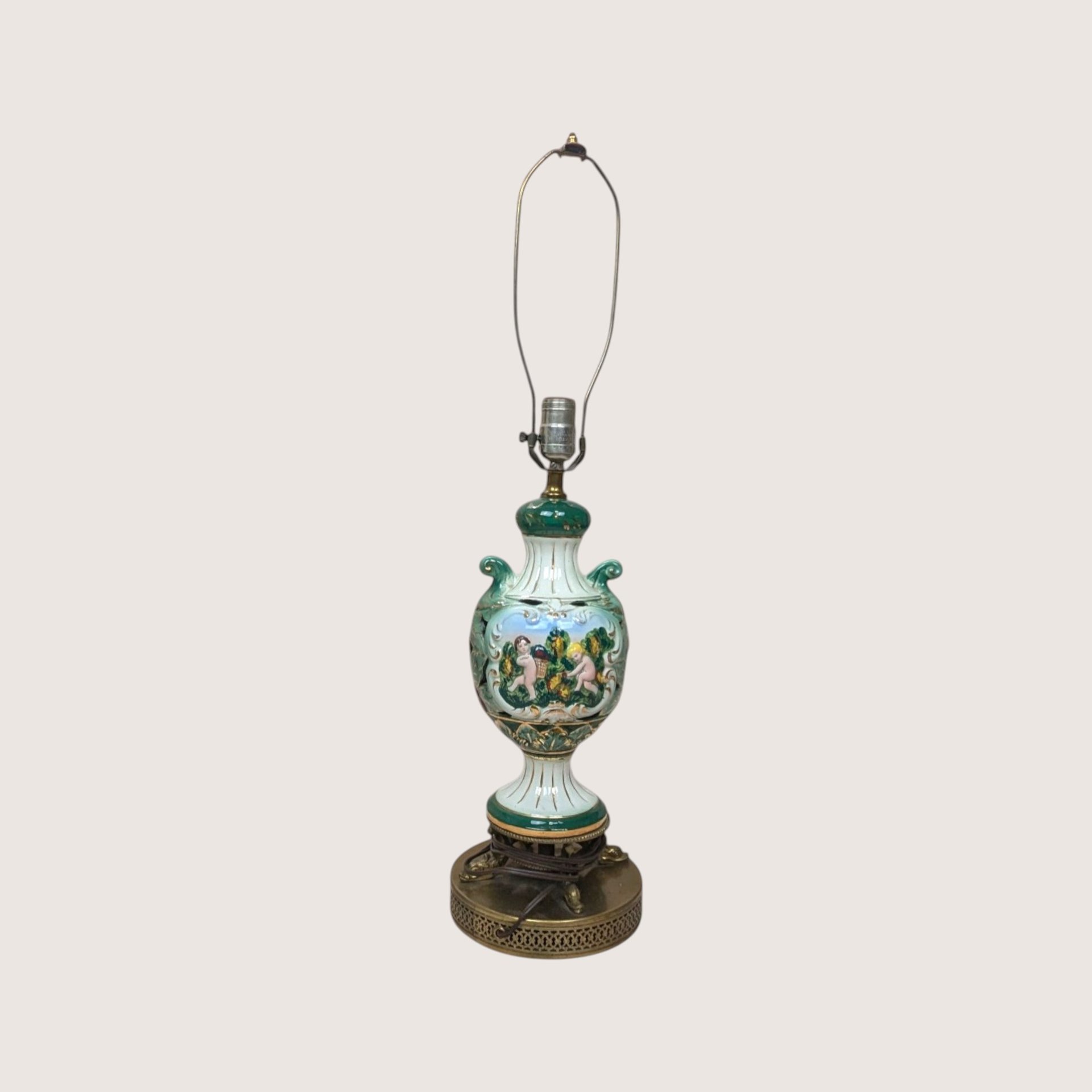A vintage Italian ceramic table lamp featuring a green and white ornate urn body painted with cherubs.