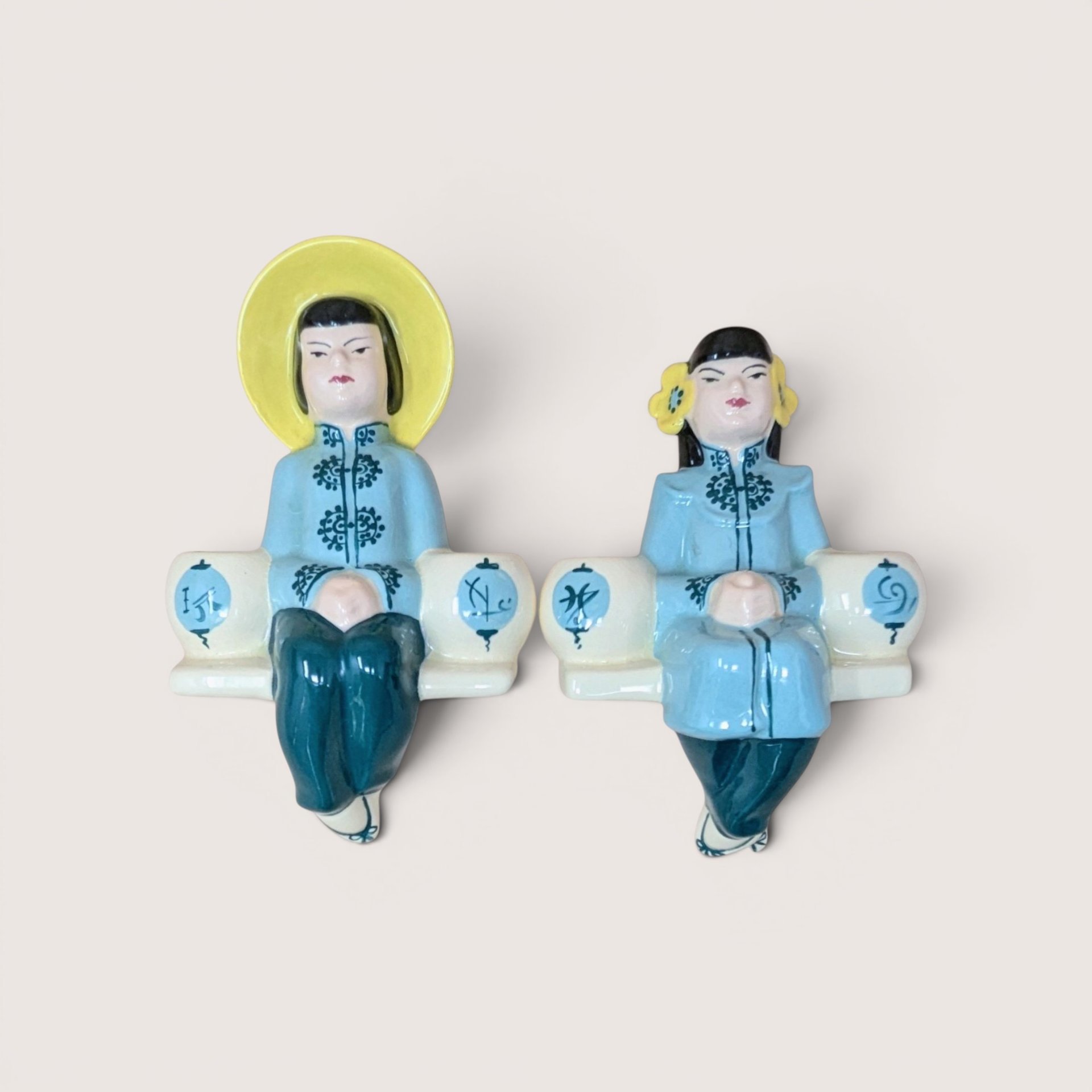 Pair of ceramic Asian-inspired shelf sitter figurines wearing light blue and teal attire, centered on a plain linen background.