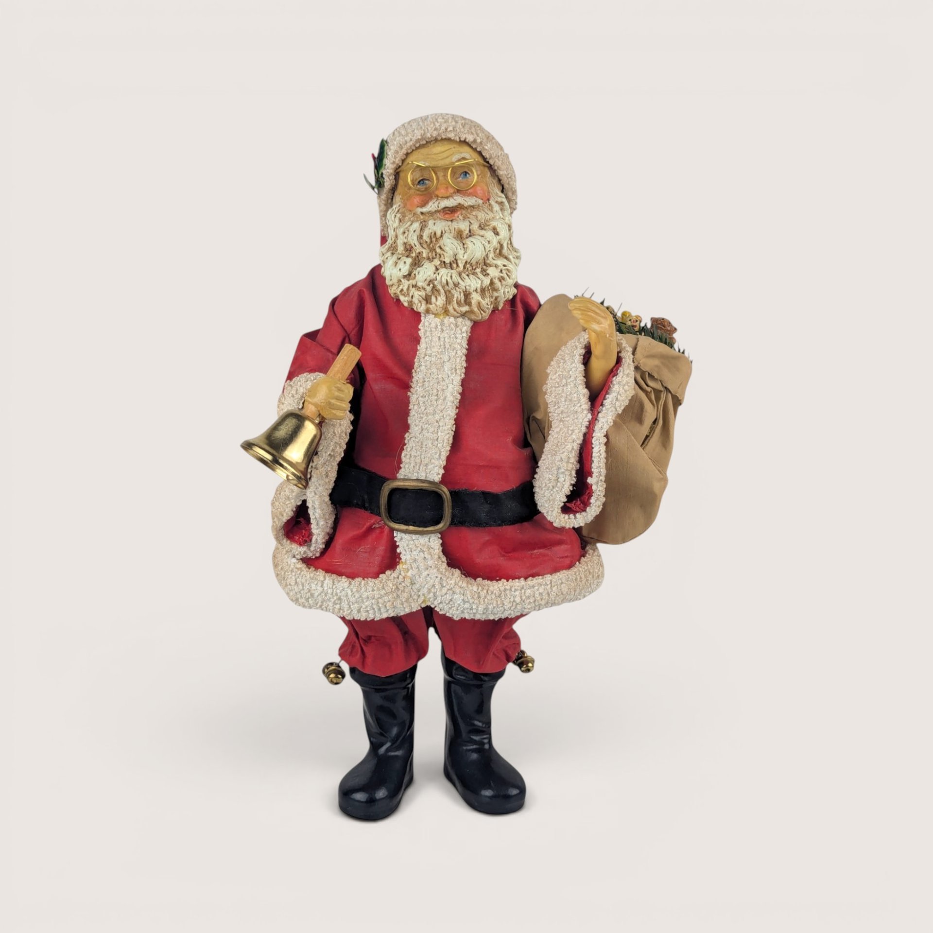 A 9.5-inch vintage Midwest of Cannon Falls Santa figurine wearing a red coat with faux fur trim, black boots, wire glasses, and holding a gold bell and a sack filled with toys.