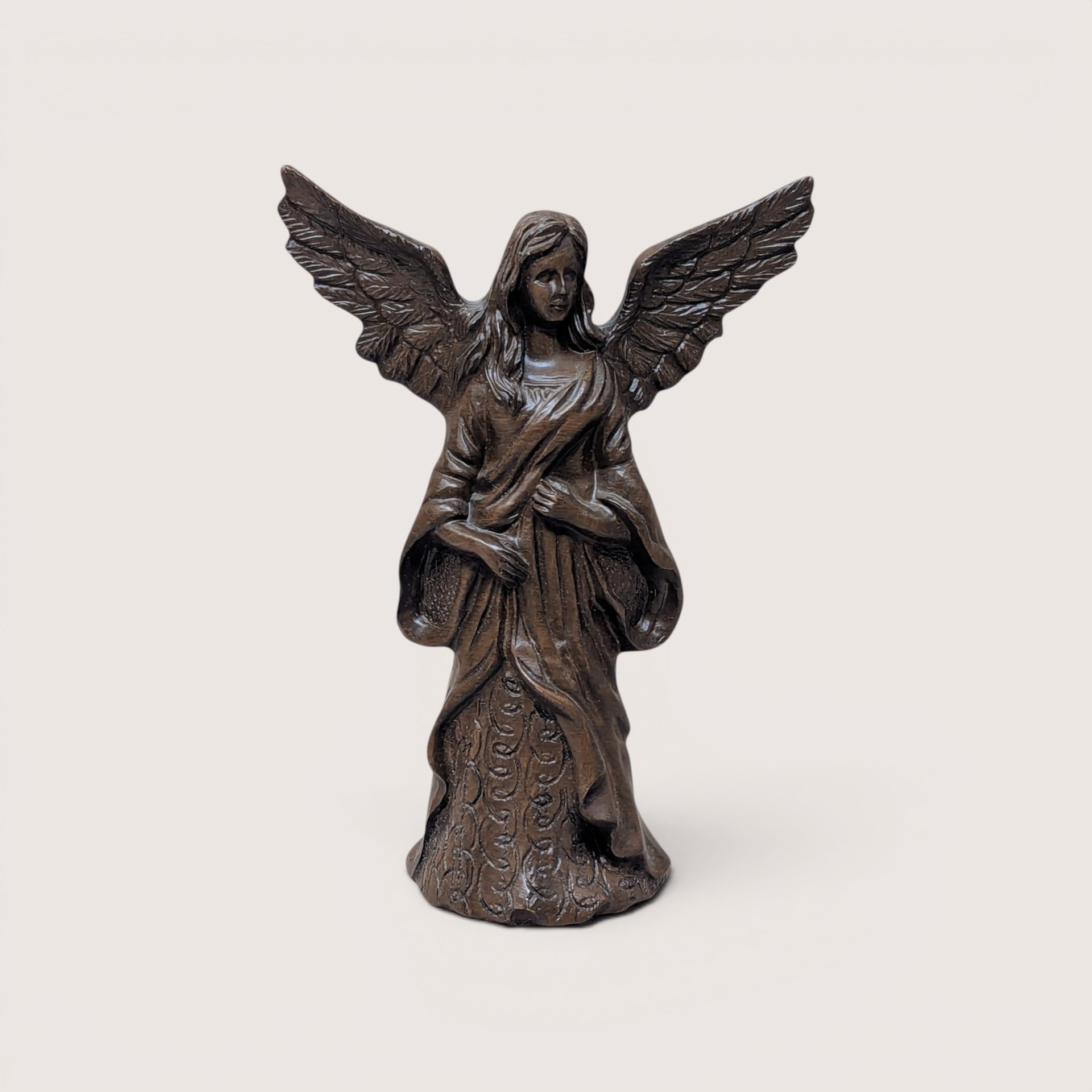 Bronze-finished angel figurine with outspread wings and a patterned gown, centered on a plain linen background.