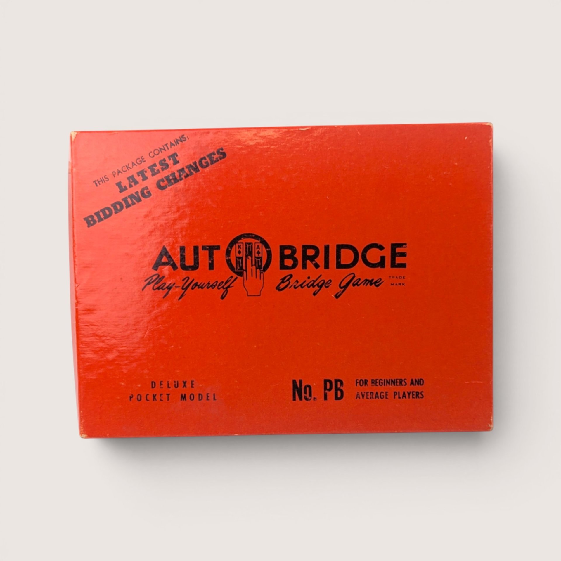 The red box lid of a 1959 vintage Auto Bridge deluxe pocket model solitaire game featuring black typography and the central logo with a hand holding cards.