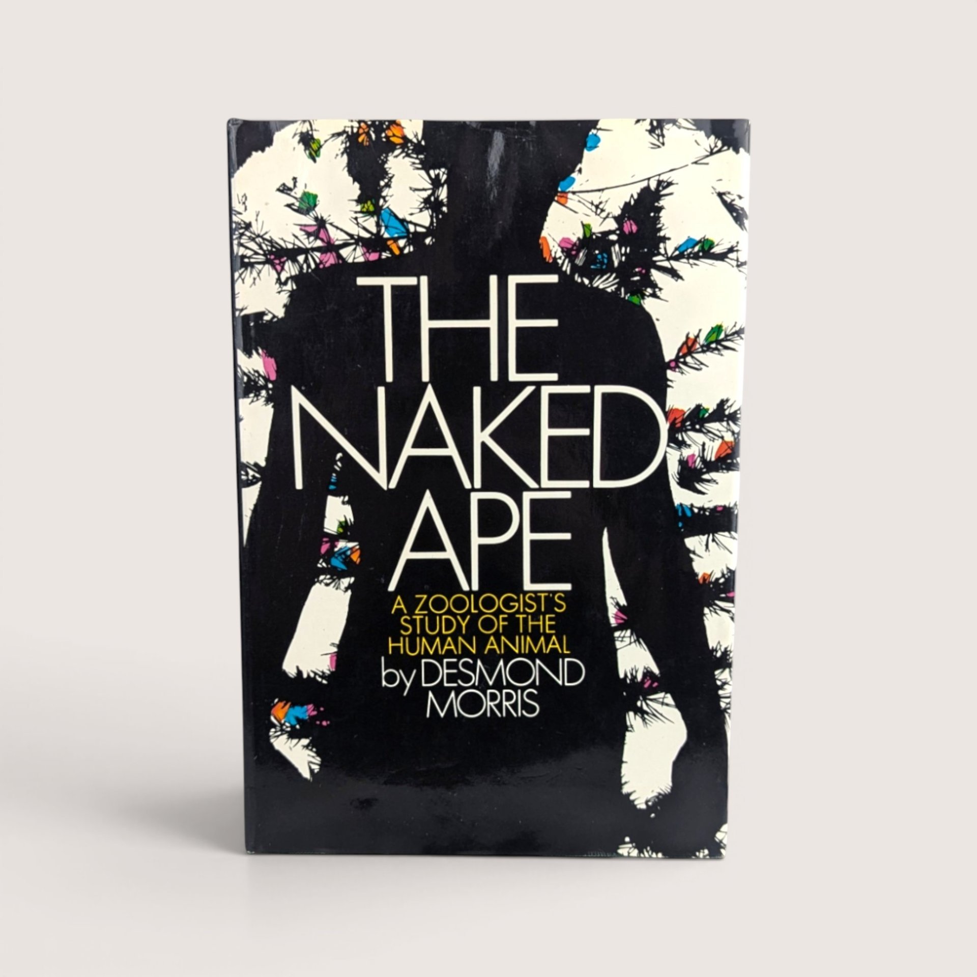 The dust jacket cover of The Naked Ape hardcover book by Desmond Morris featuring a black silhouette with colorful abstract accents.