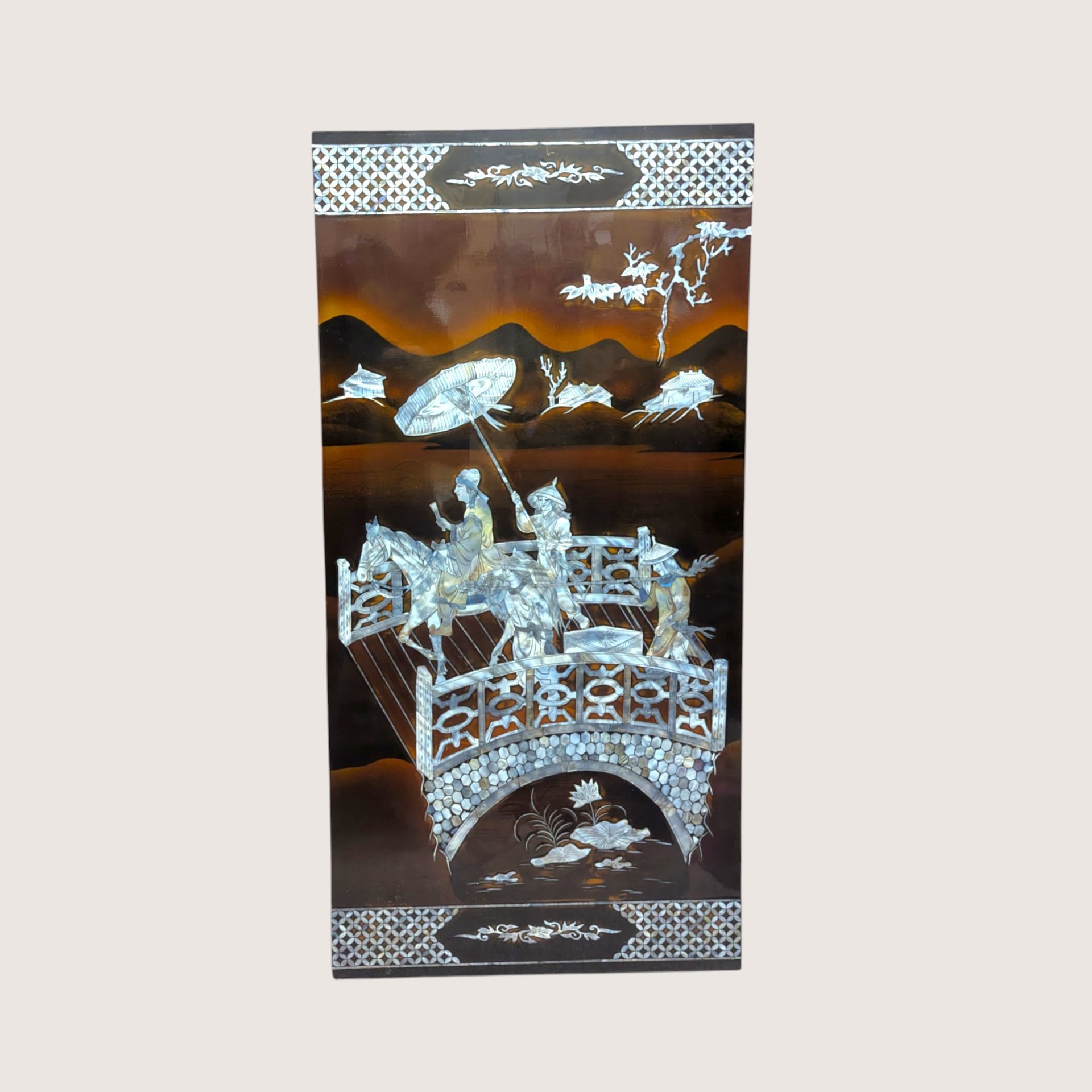 A large rectangular black lacquer wall panel featuring a detailed mother of pearl inlay scene with figures on a bridge.