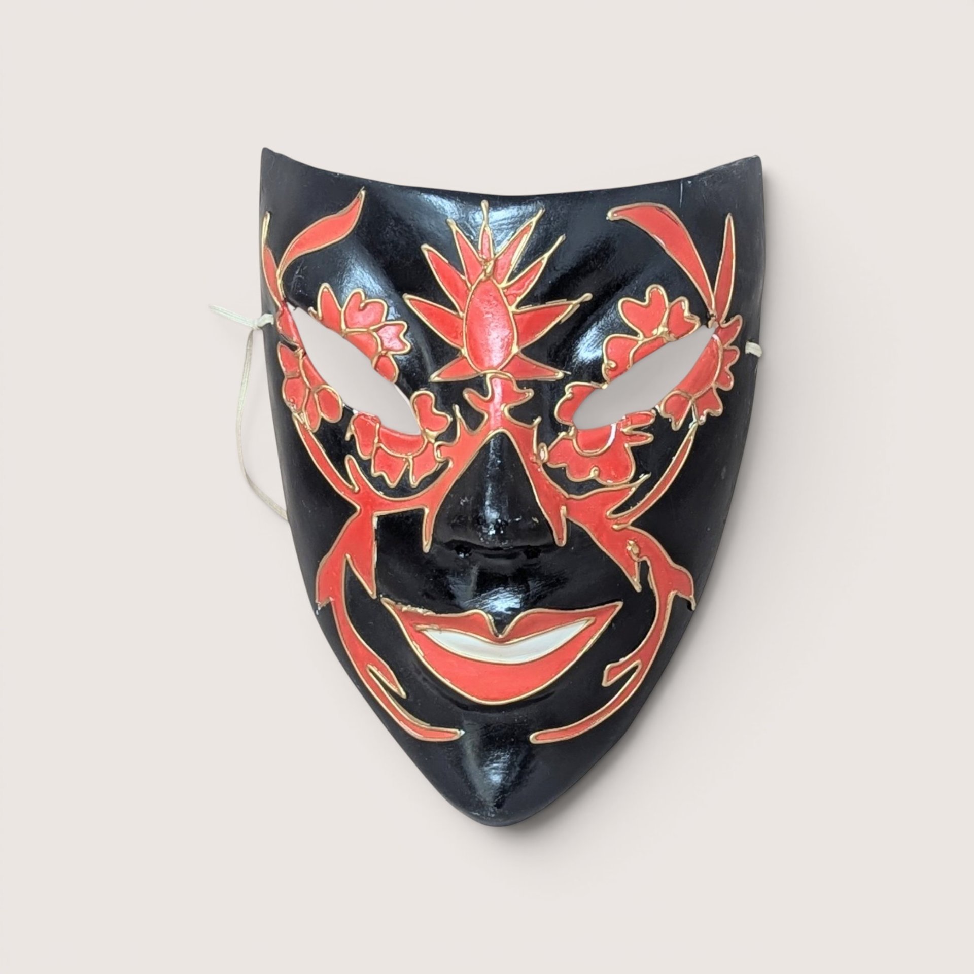 Black lacquer decorative masquerade mask featuring hand-painted red floral patterns and gold accents around the eyes, forehead, and lips, centered on a plain linen background.