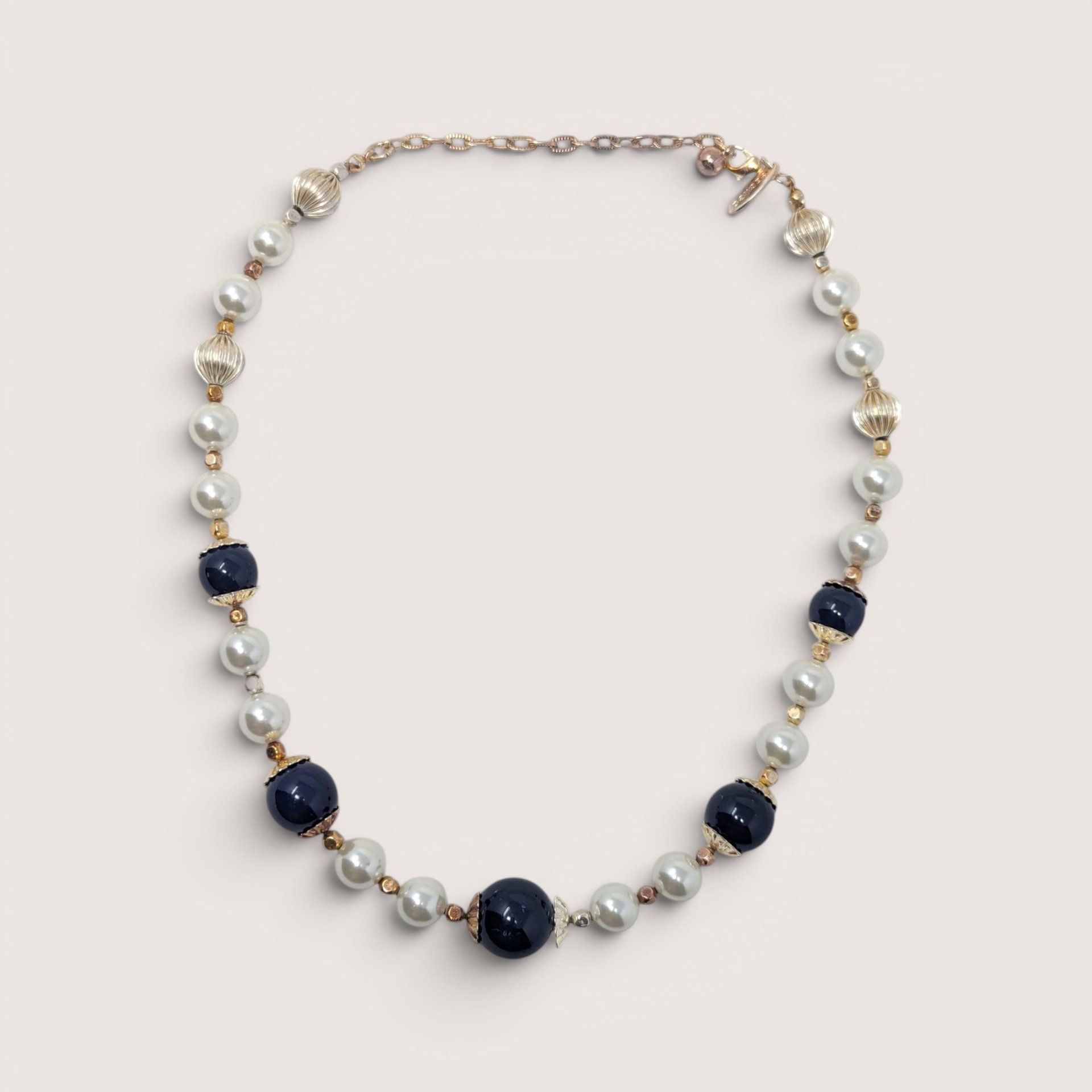 Vintage George statement necklace with dark blue glass beads, white pearls, and gold accents on a linen background
