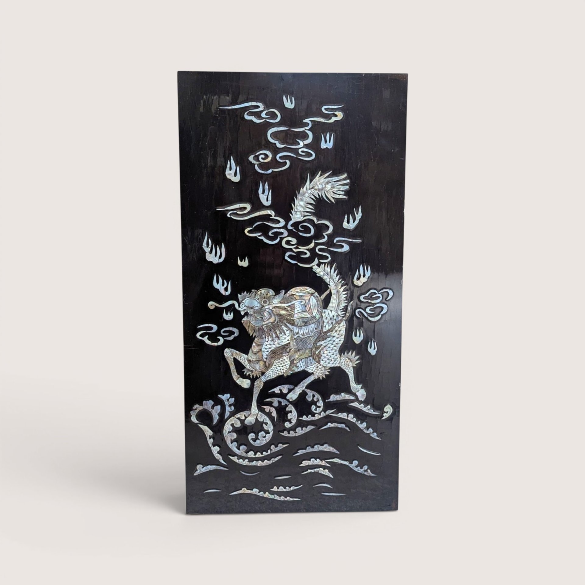Vintage Asian black lacquer wood wall panel with iridescent mother of pearl inlay depicting a qilin on a linen background