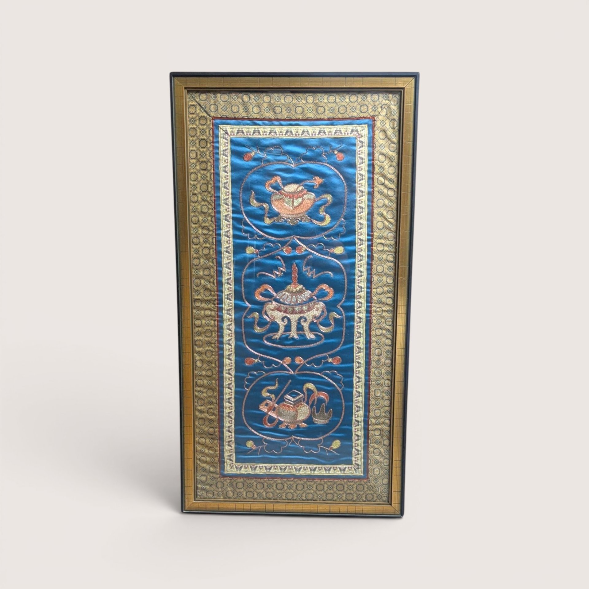 Vintage framed Chinese silk embroidery panel with three urn and censer motifs on a blue background and a linen backdrop