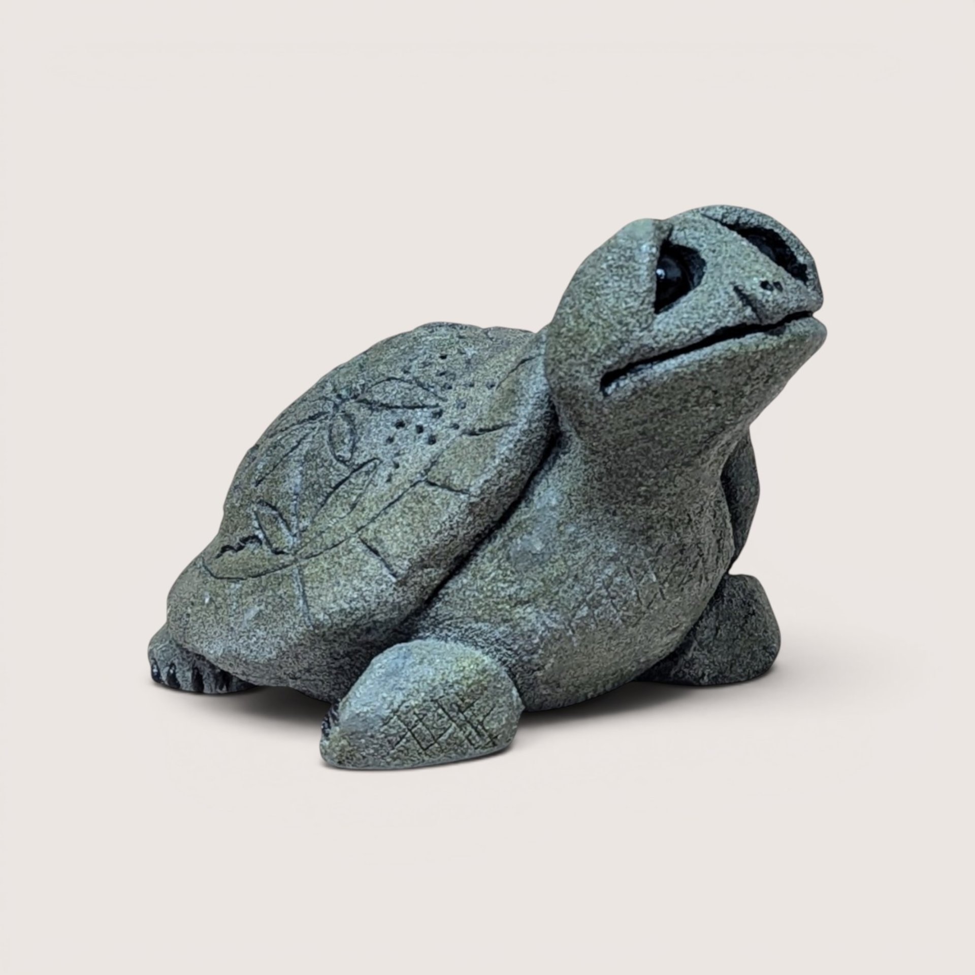 Vintage cast stone or resin turtle figurine with a textured, gray-green finish, featuring a stylized leaf pattern etched into its shell and its head tilted upward, centered on a plain linen background.